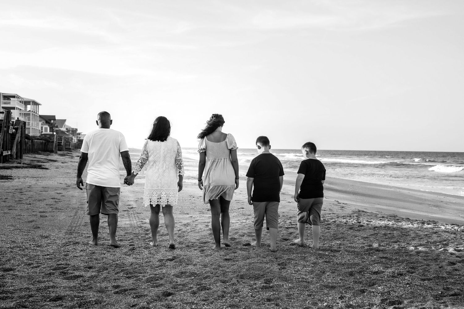 Family of five walking hand in hand toward the ocean, black and white, Jacksonville, FL