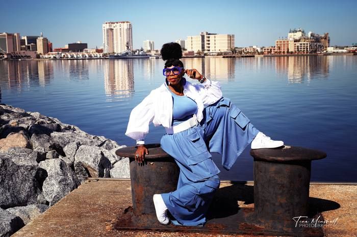 Woman in a blue jumpsuit posing on a waterfront dock with the Jacksonville skyline behind her, women's portrait session.