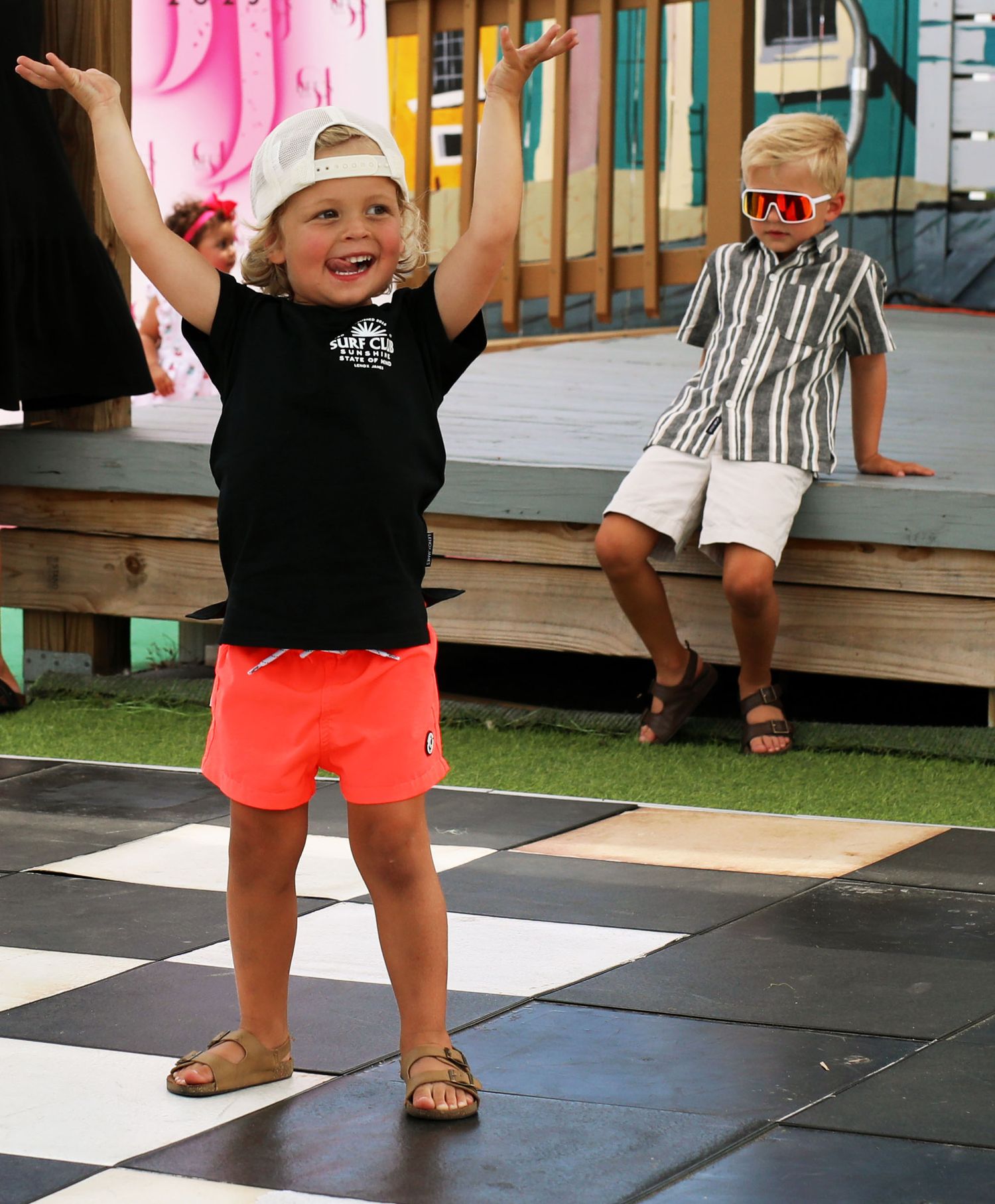 Toddler celebrating with arms raised on a checkered floor, joyful candid portrait
