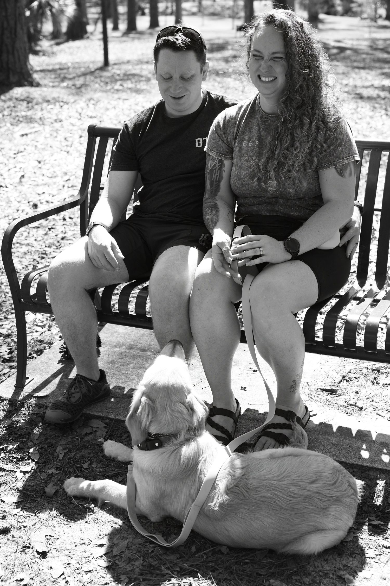 Black and white candid of a couple laughing on a park bench with their dog