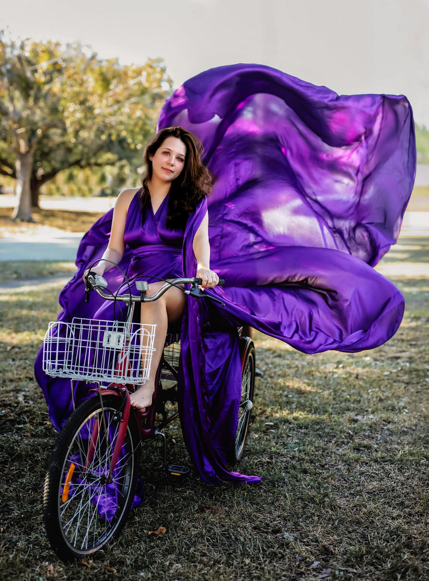 Woman in a purple flying dress riding a bicycle, fabric flowing behind her