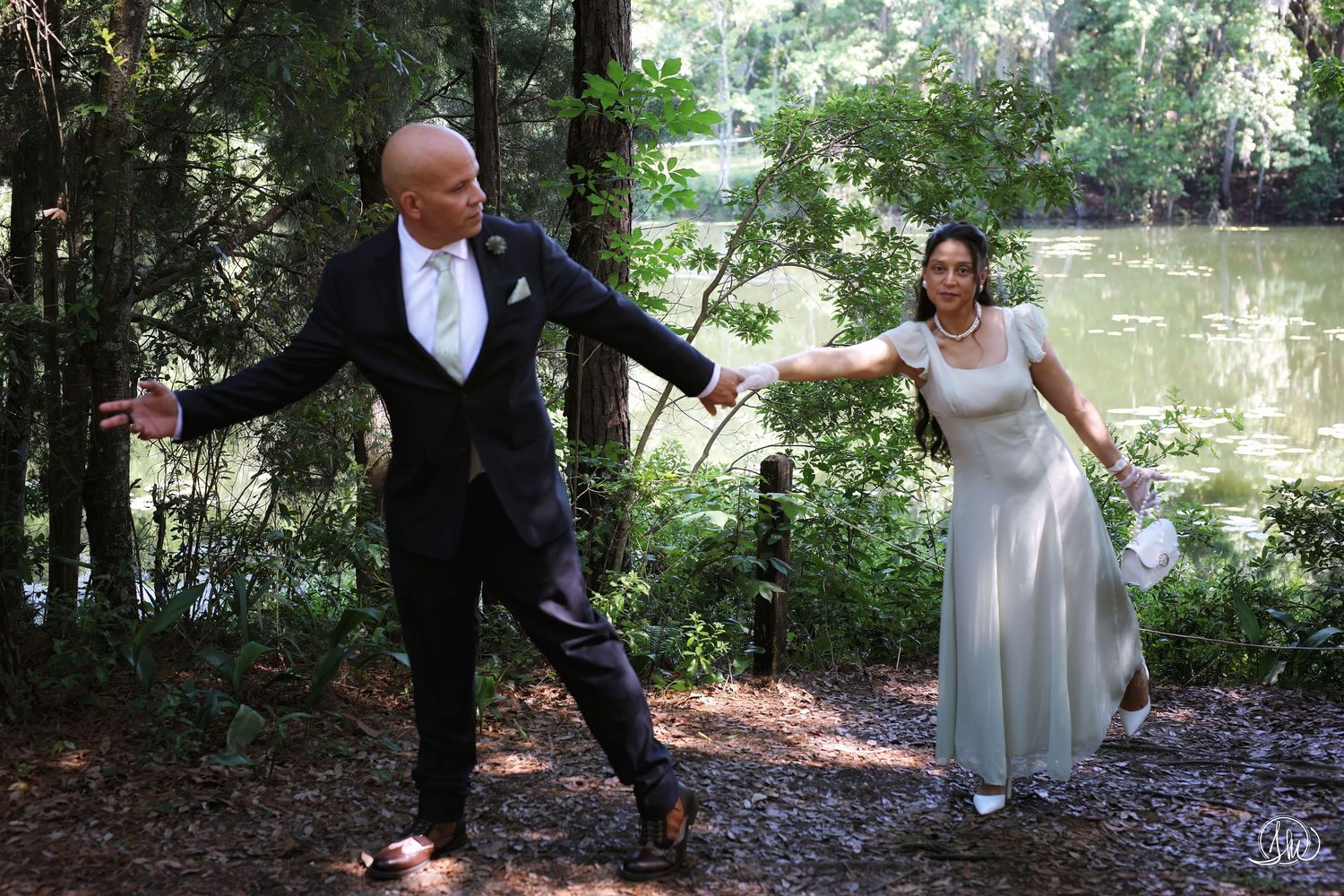 Couple in formal attire holding hands mid-step near a wooded pond, editorial portrait session in Jacksonville, FL