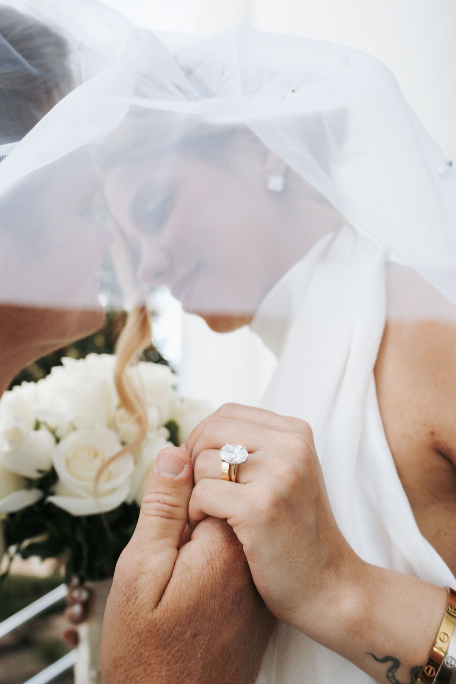 Bride and groom share a kiss under a white veil, showcasing a stunning gold diamond engagement ring.