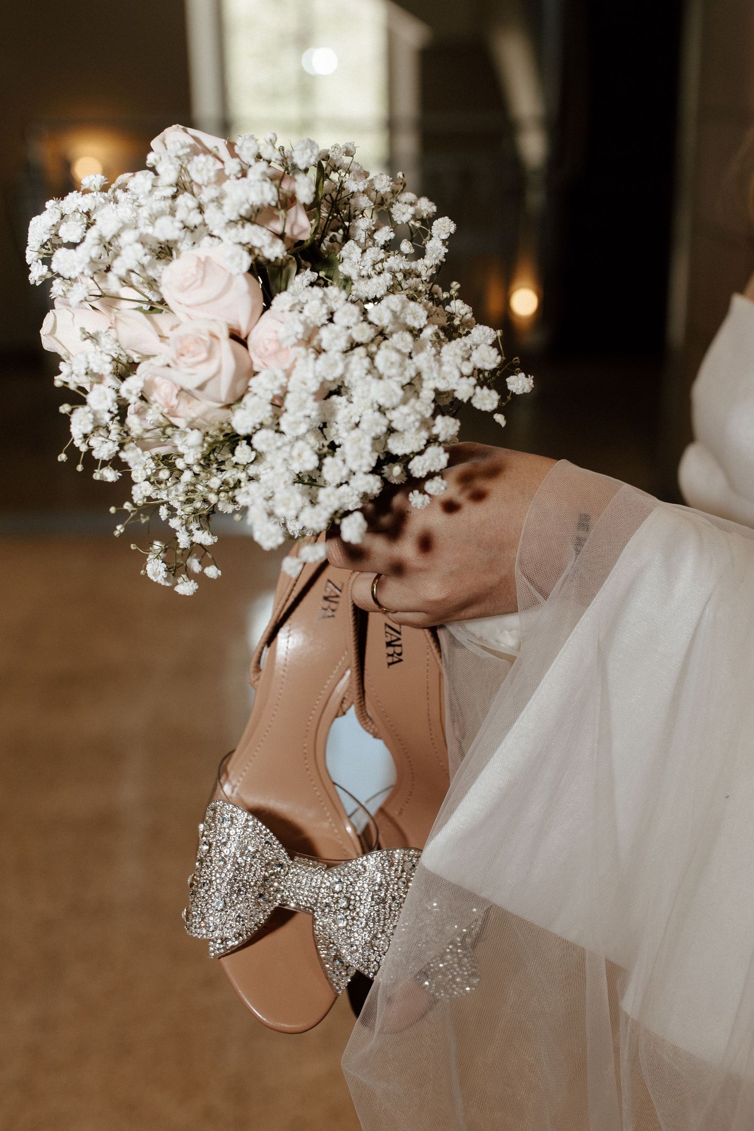 Bridal heels with crystal bow detail beside a delicate pink rose and baby's breath wedding bouquet.