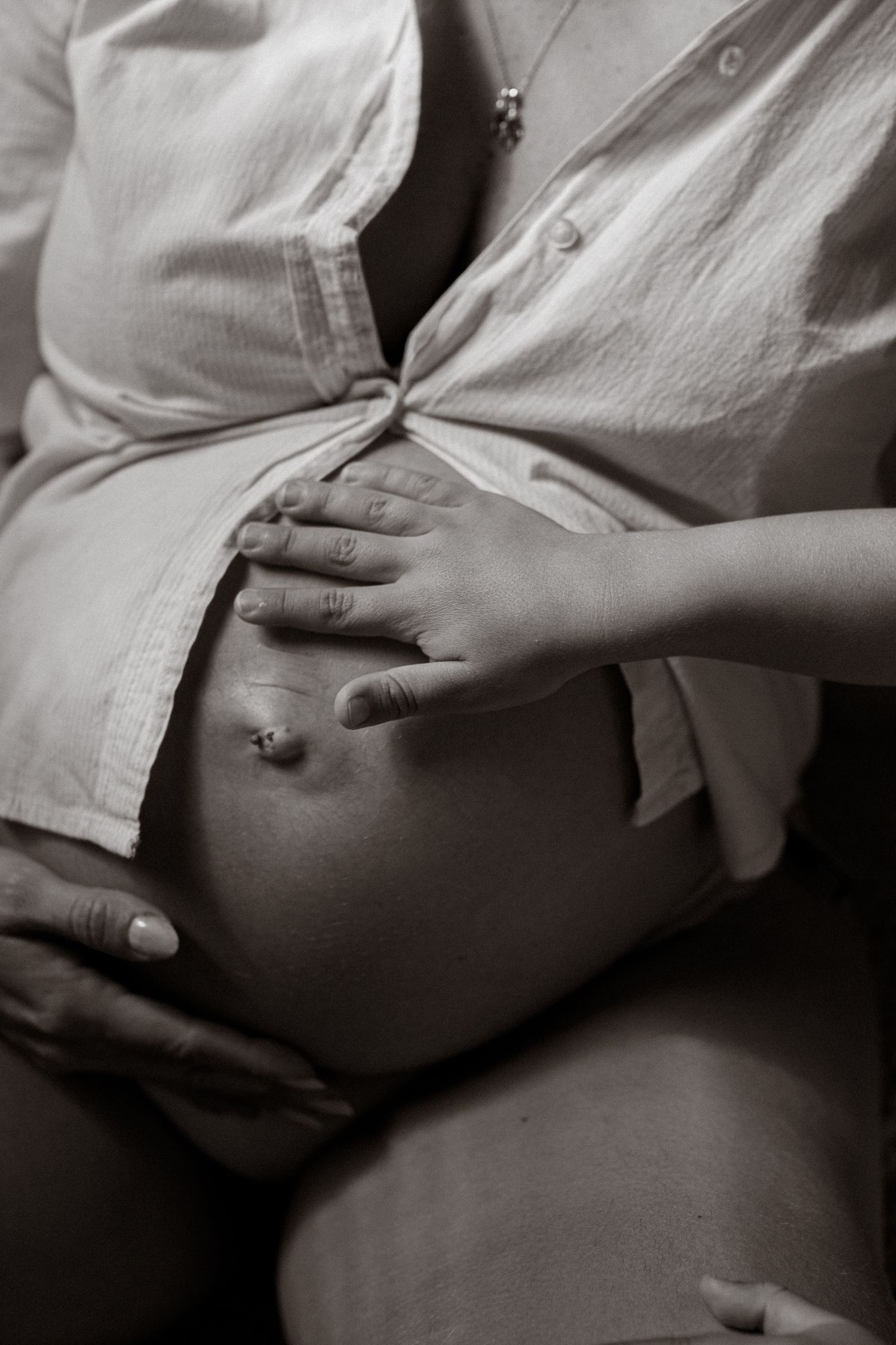 Black and white close-up of pregnant woman cradling bare baby bump with both hands.