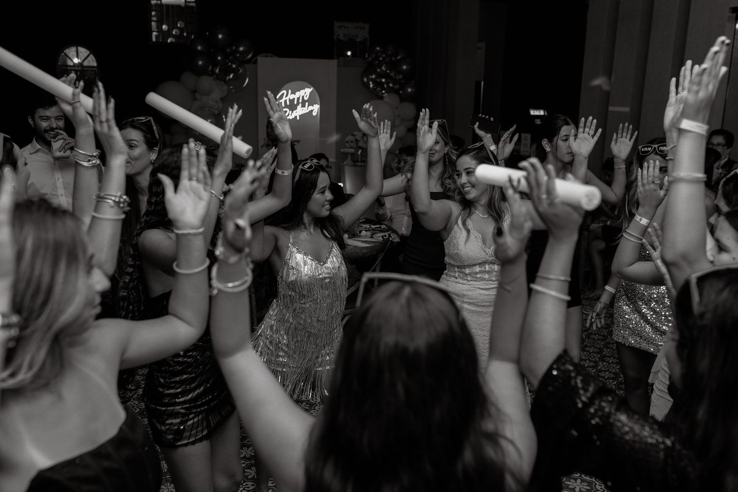 Black and white photo of women dancing with hands raised at a lively party event.
