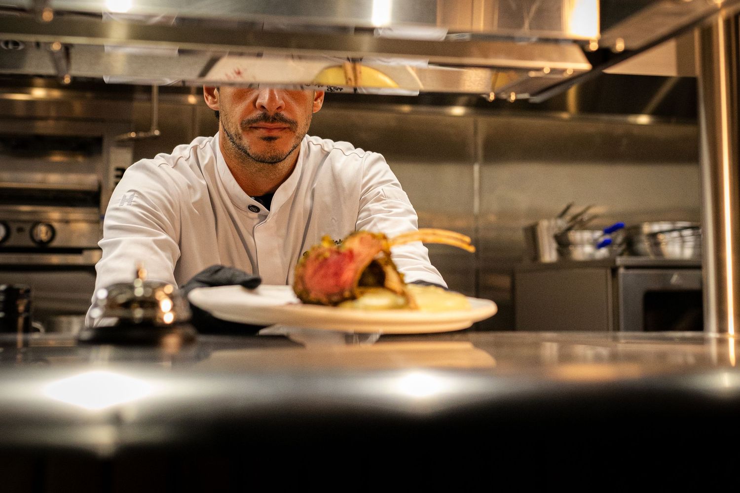 Male chef in white coat plates a gourmet meat dish in a professional restaurant kitchen.