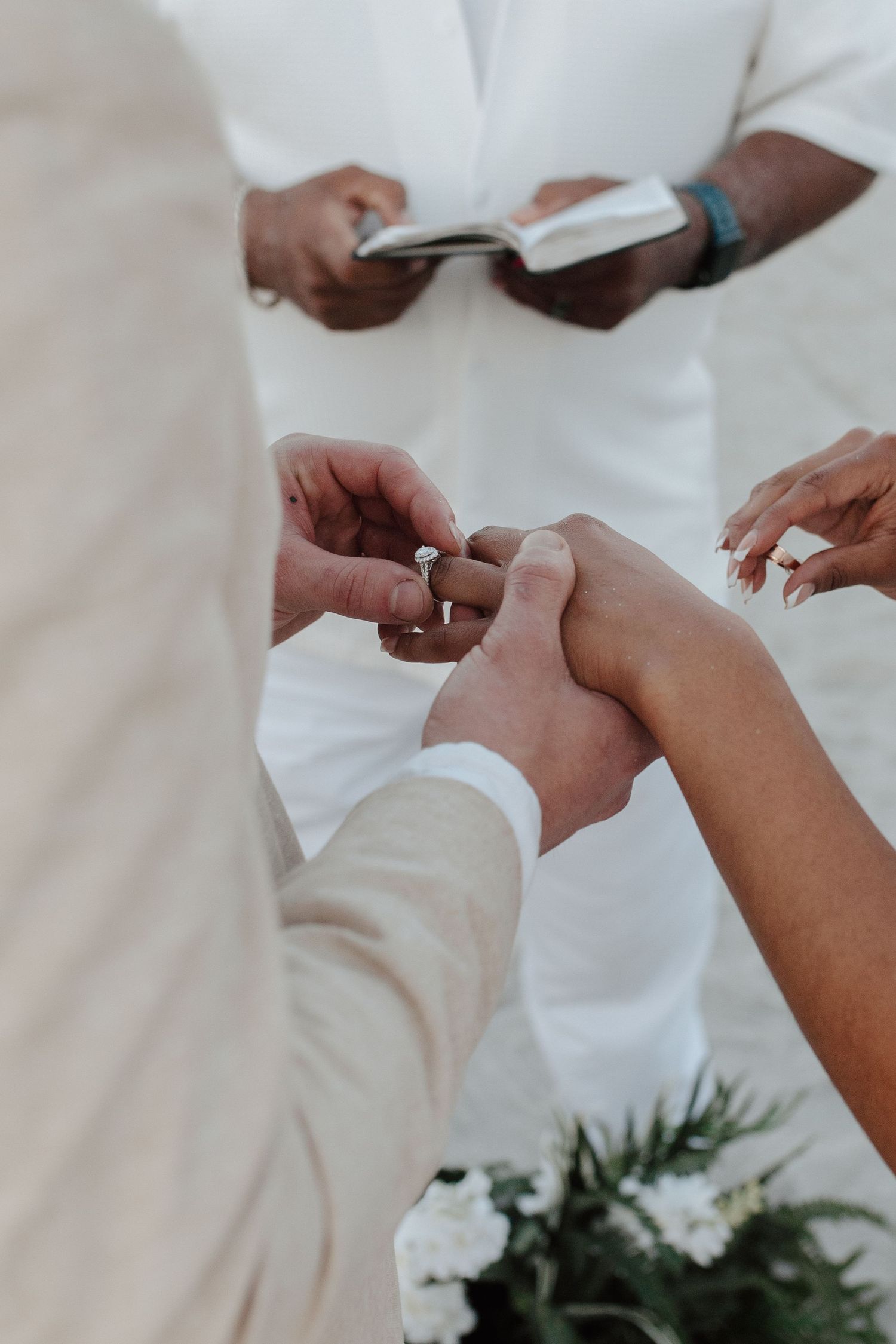 Close-up of a groom sliding a diamond ring onto his brides finger during a beach wedding ceremony.