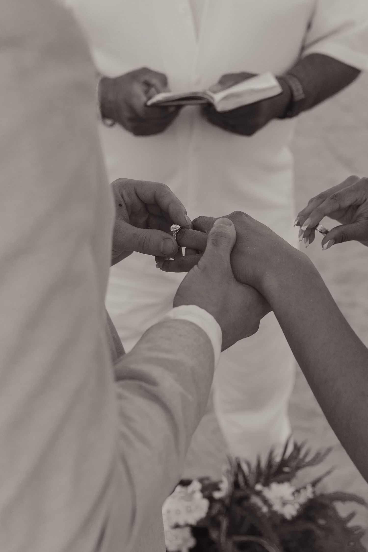 Black and white photo of groom placing wedding ring on brides hand during beach ceremony.