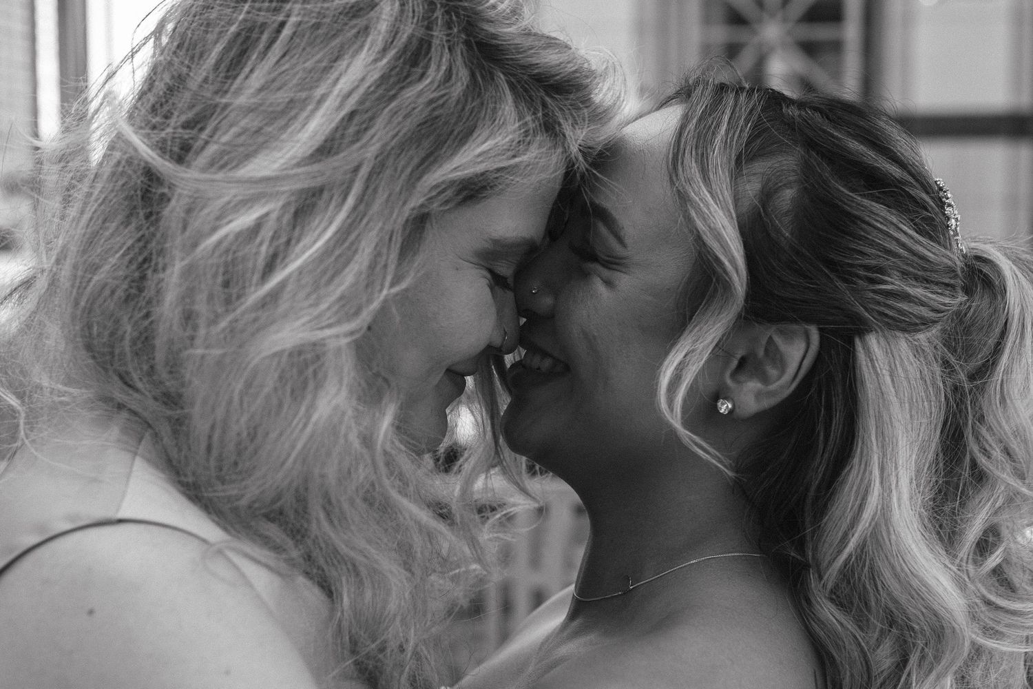 Black and white close-up of two blonde women sharing a romantic kiss at a wedding celebration.