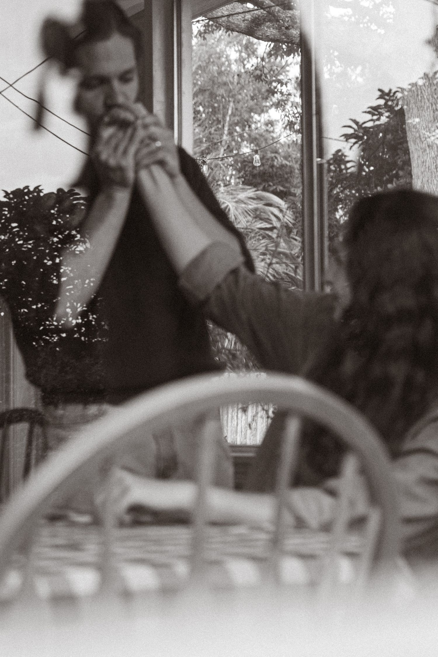 Black and white candid photo of a couple sharing a moment at a dining table near a window.