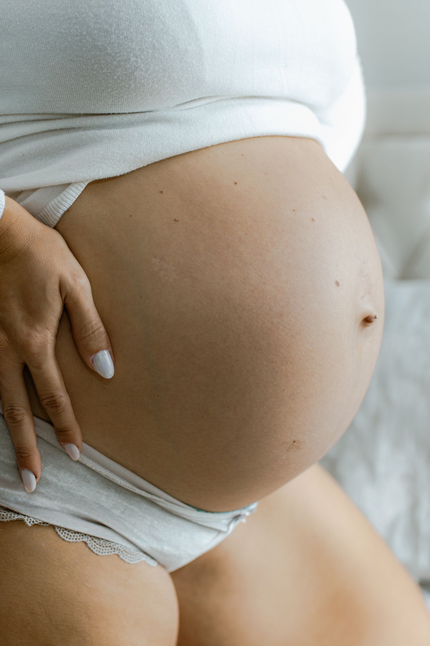 Close-up of pregnant woman in white top gently holding her bare baby bump.