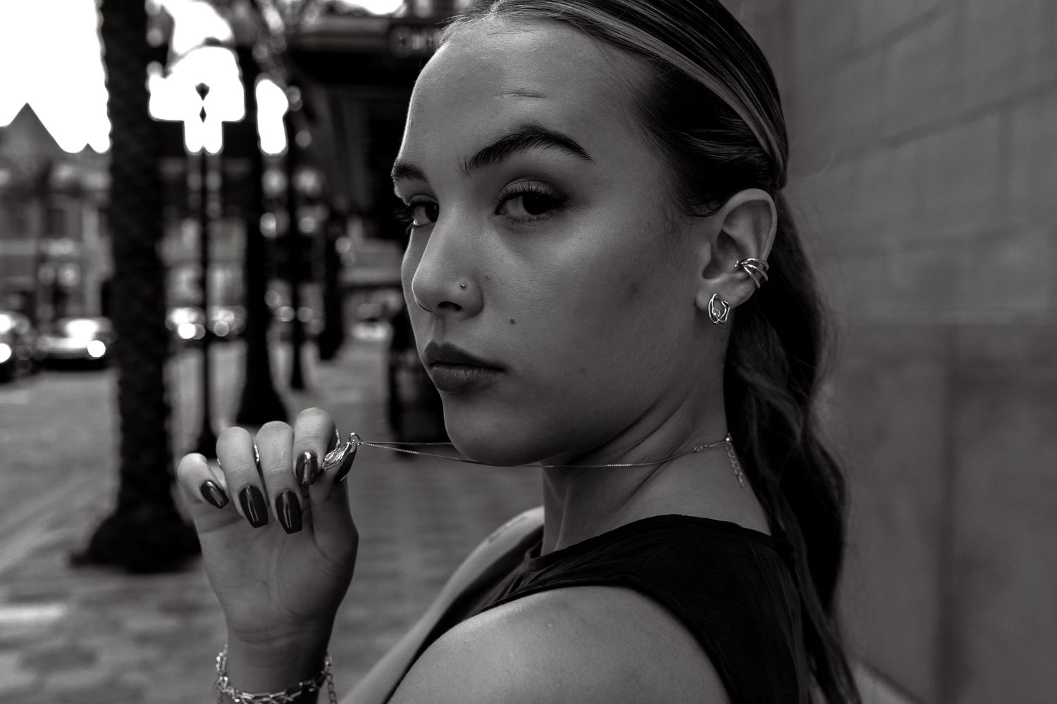 Black and white portrait of young woman with ear cuff posing on urban street.