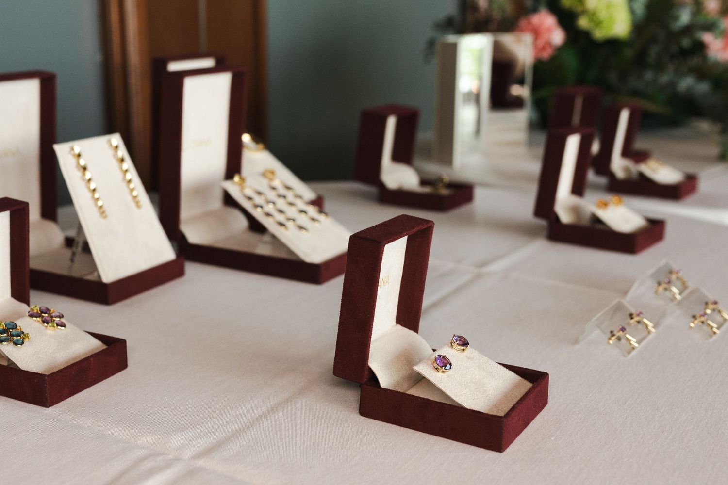 Elegant jewelry display in burgundy velvet boxes arranged on white tablecloth.