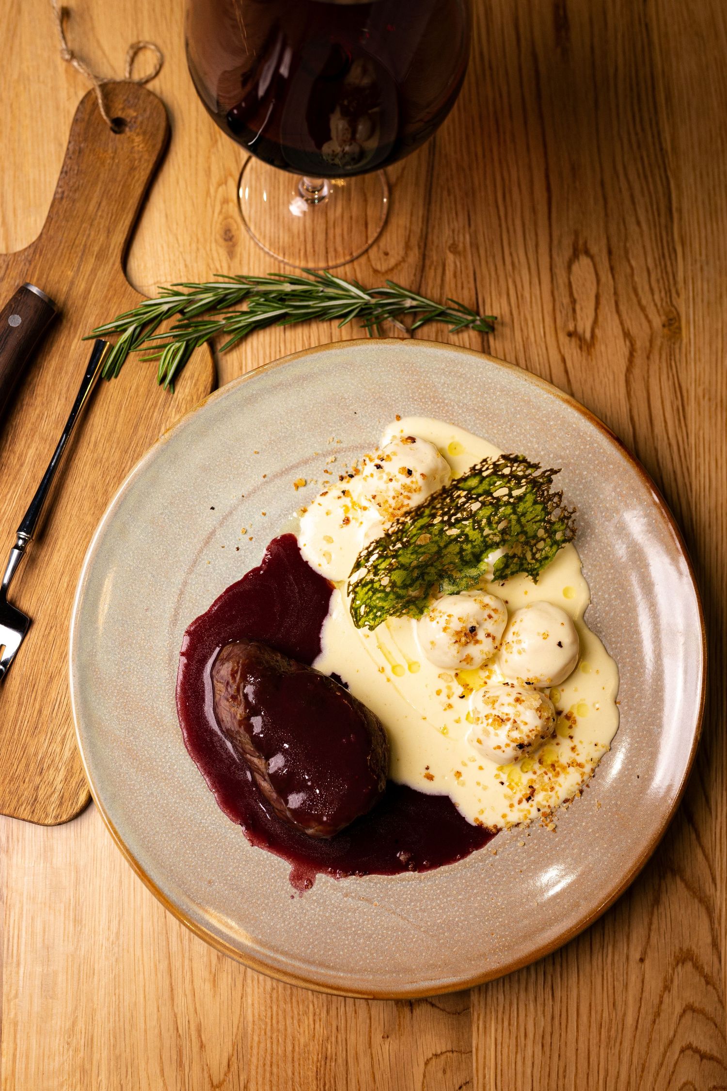 Gourmet beef dish with red wine sauce, mashed potatoes, and asparagus served on a ceramic plate with wine.