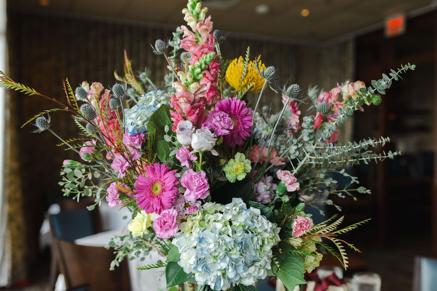 Colorful wildflower bouquet with pink gerberas, hydrangeas, snapdragons, and eucalyptus in a vase.