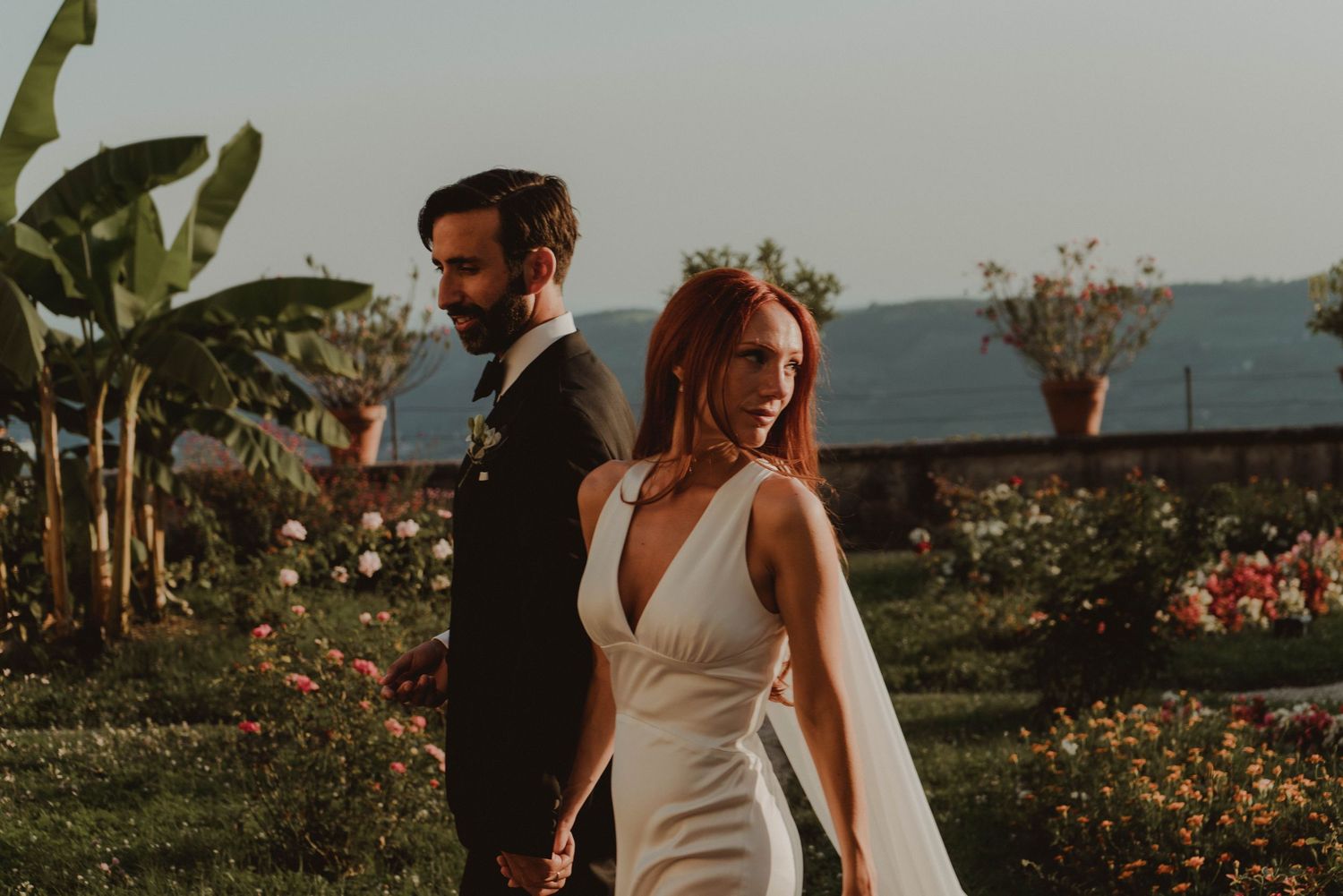 Newlywed couple with the bride looking back, surrounded by the beautiful gardens of a villa in the countryside near Verona, Italy.