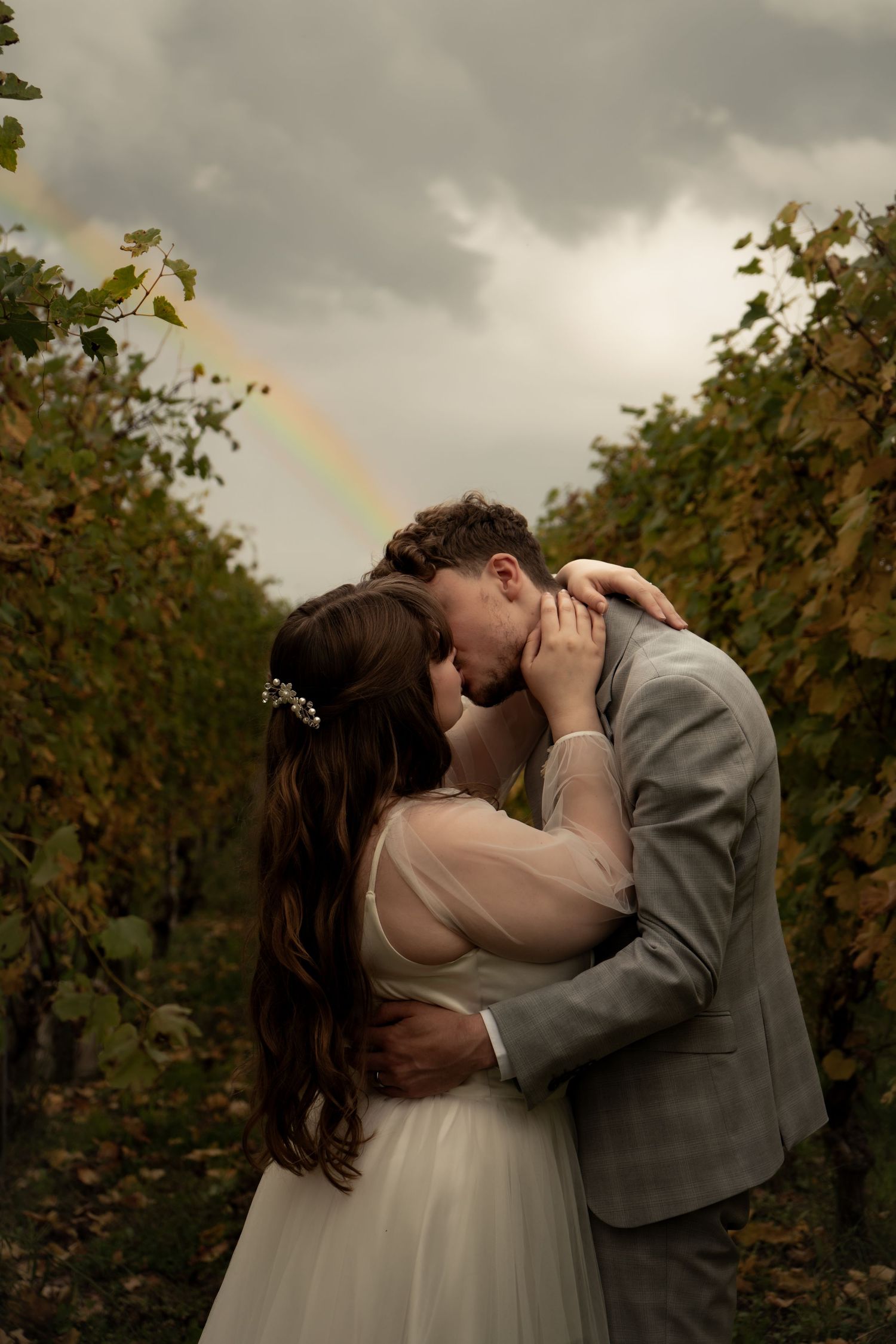 Newlywed couple kissing in the Langhe, Italy, with a rainbow in the background.