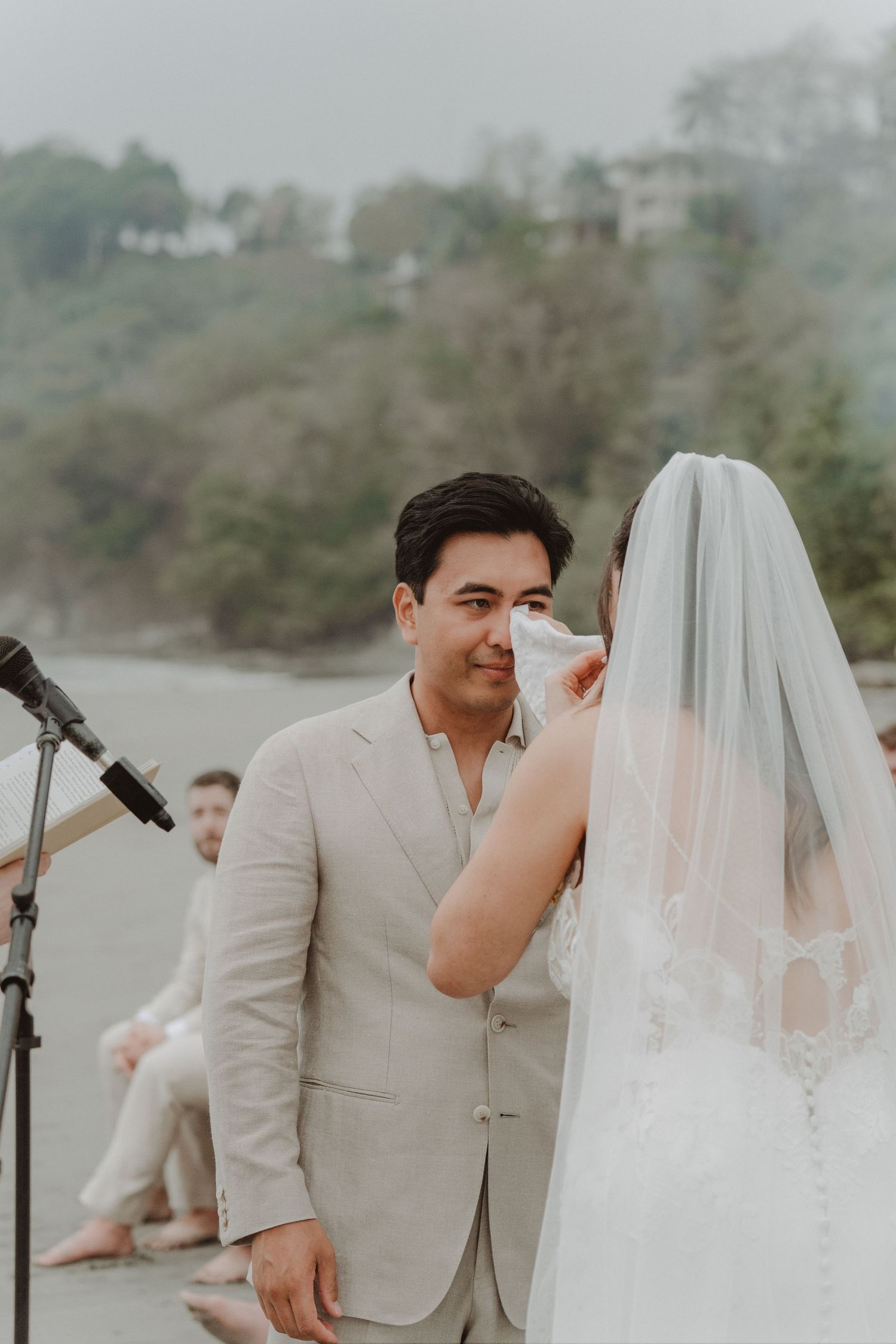 Groom wiping away tears as his bride reads her vows during their beach wedding ceremony.