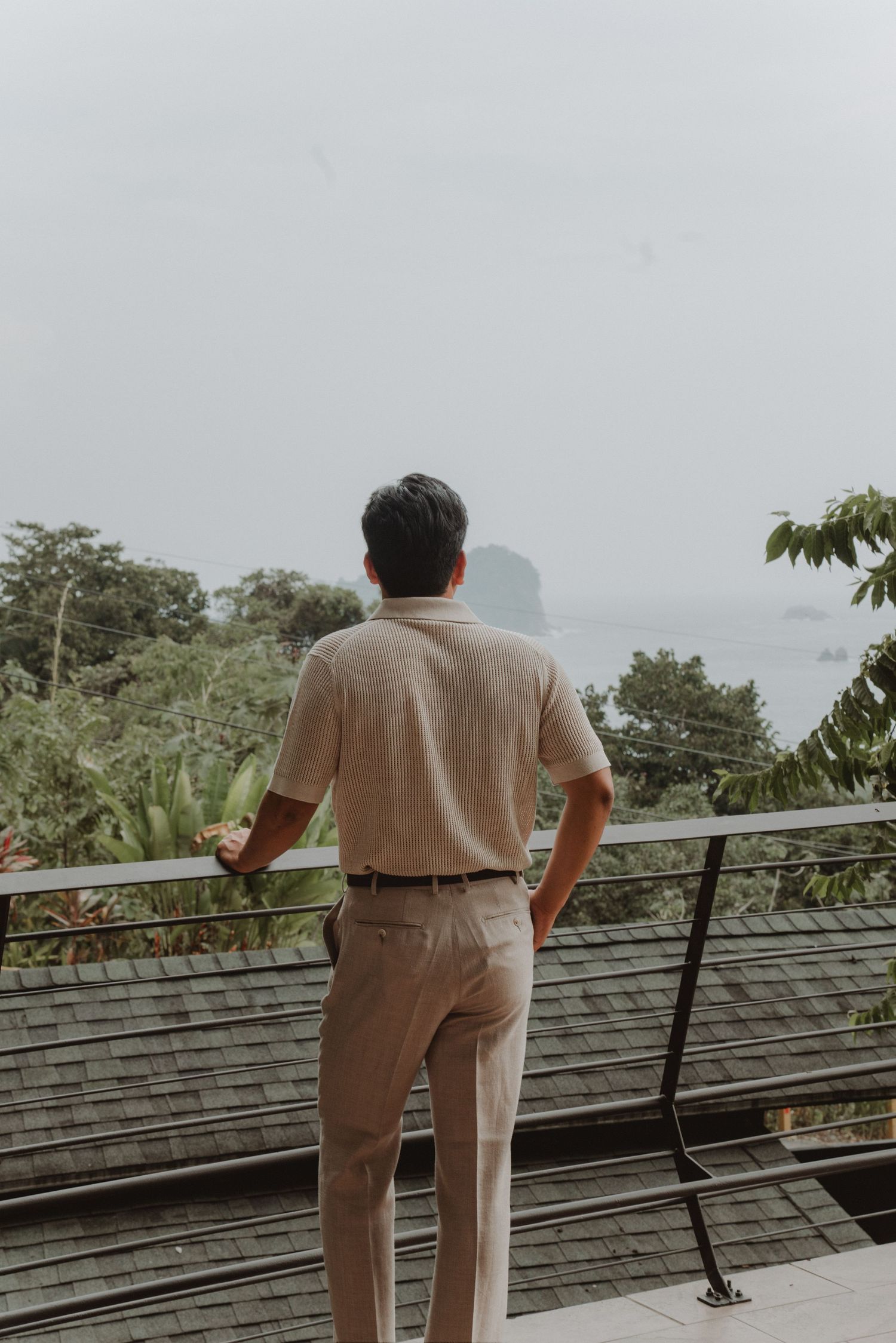 Groom standing on a terrace overlooking the sea, seen from behind, on his wedding day.