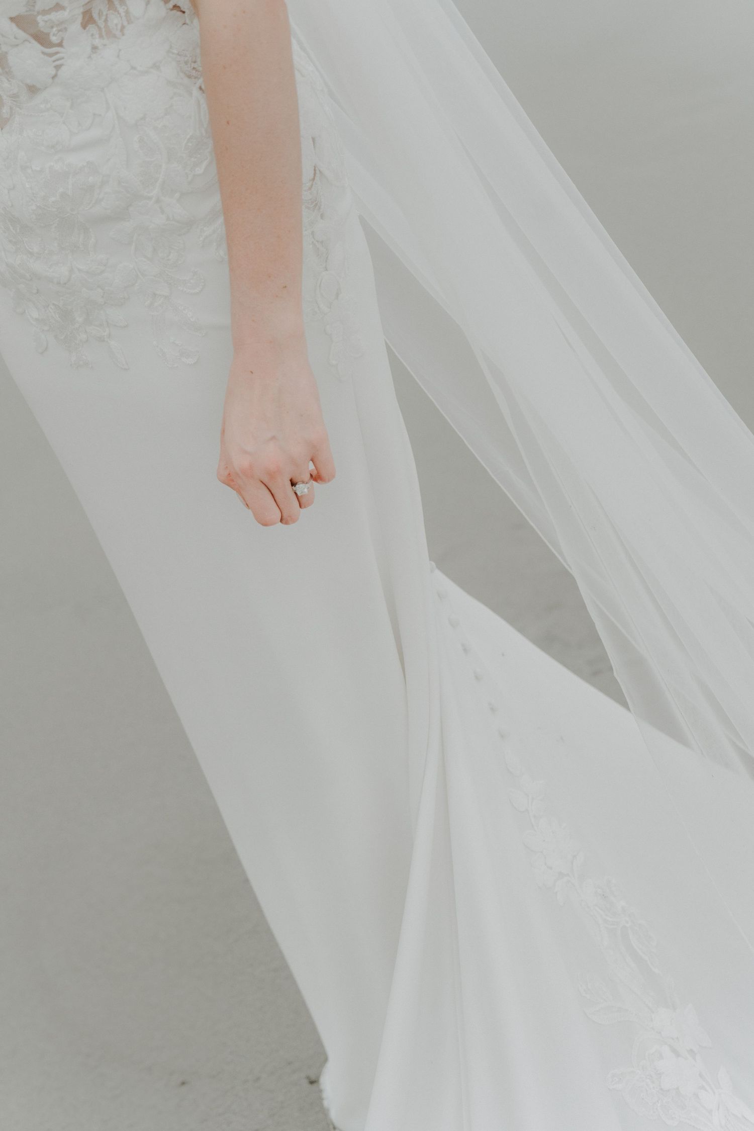 Detail of the bride's wedding dress and ring with the beach in the background.