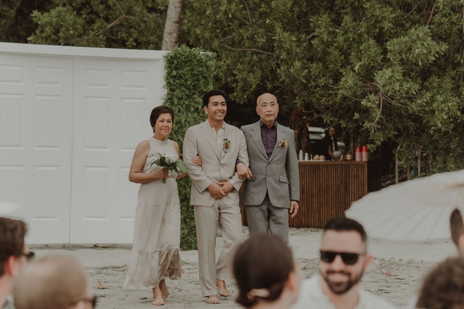 Groom walking down the aisle with his mother and father during a beach wedding ceremony.