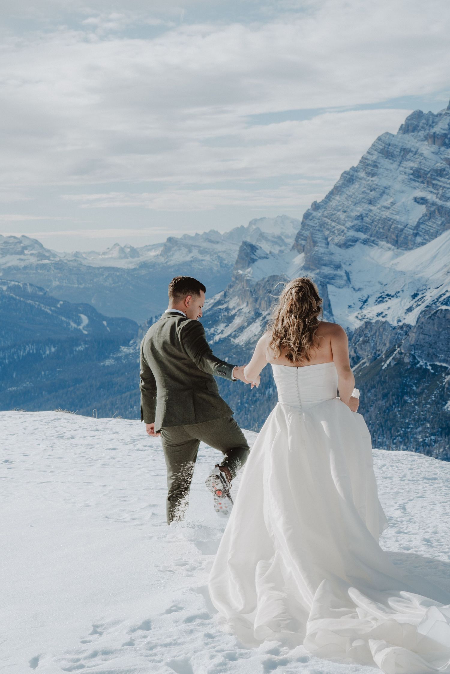 Newlywed couple walking through the snow on a mountaintop.