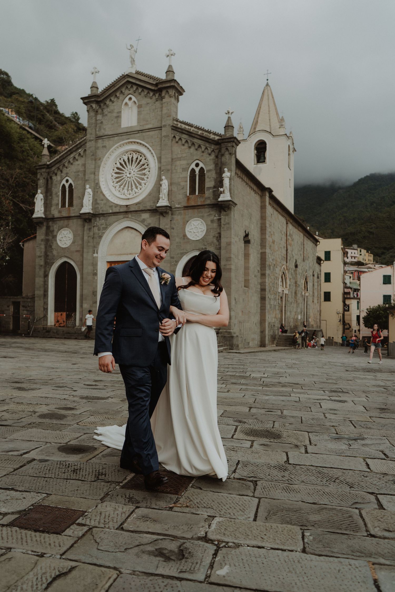 Newlywed couple holding hands and walking away from the church in Riomaggiore, Italy.