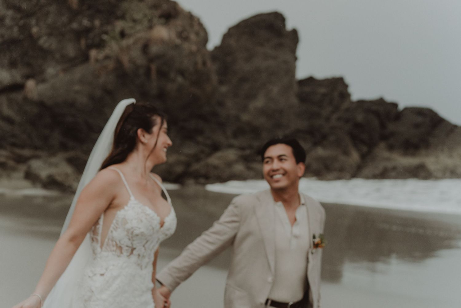 Newlywed couple running together along the beach on their wedding day.