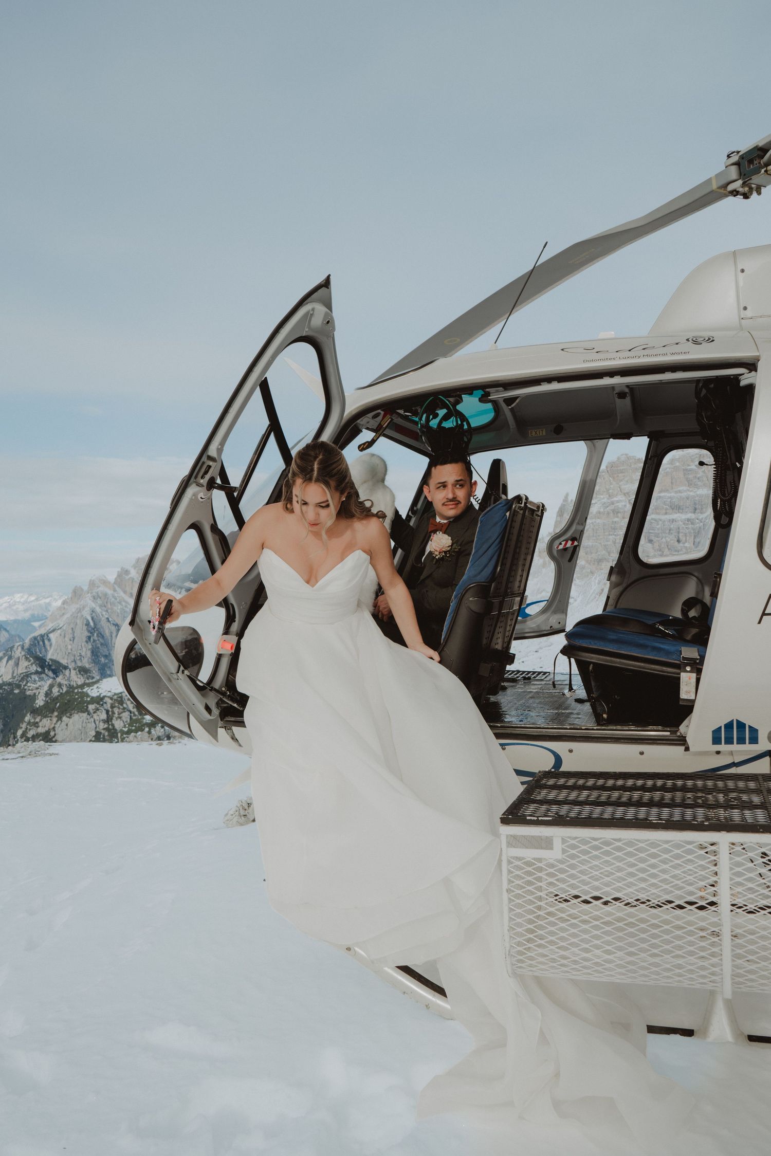 Newlywed couple stepping out of a helicopter on a snow-covered mountaintop in the Dolomites.