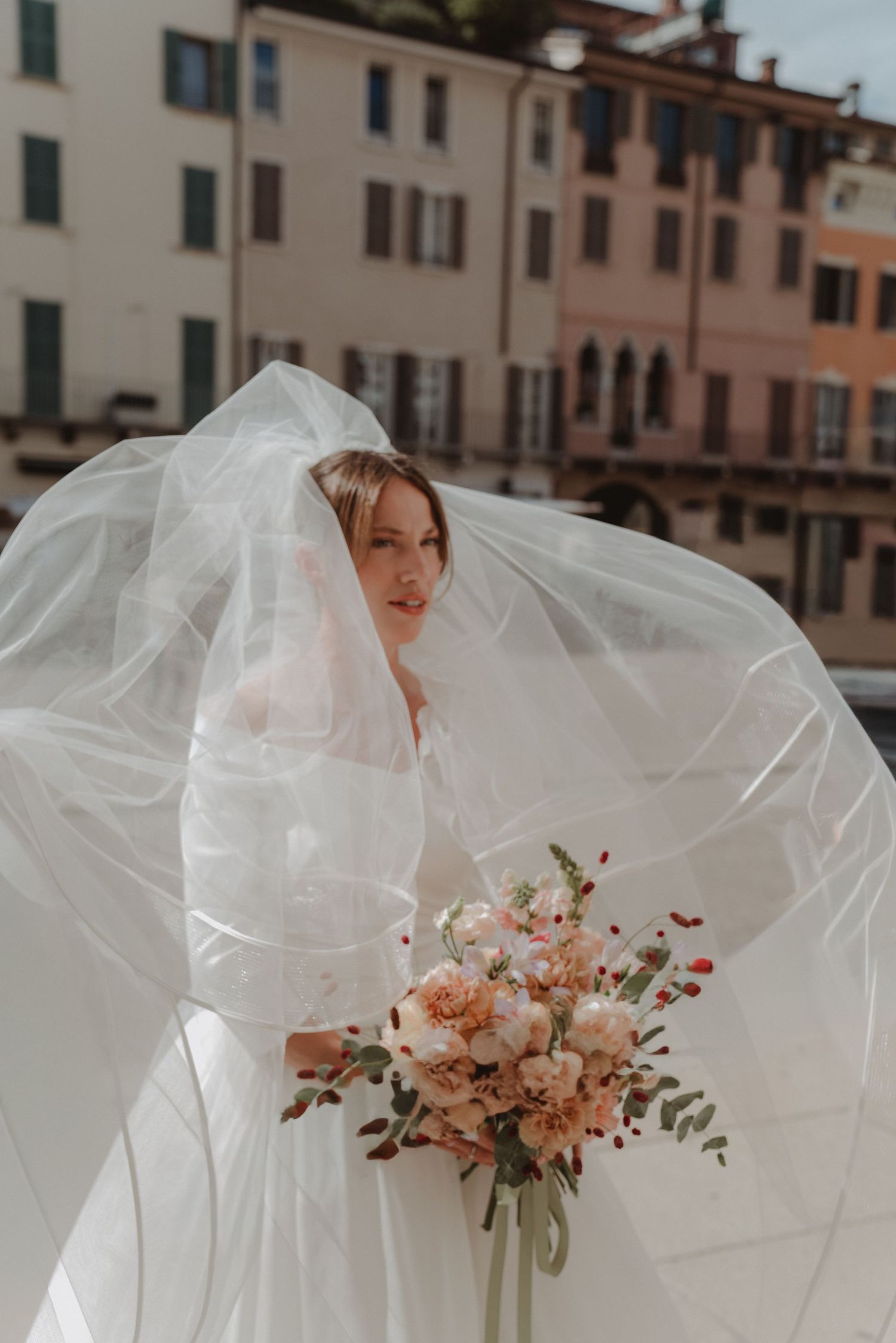 Bride holding her bouquet in Piazza Duomo in Brescia, with her veil flowing in the wind.