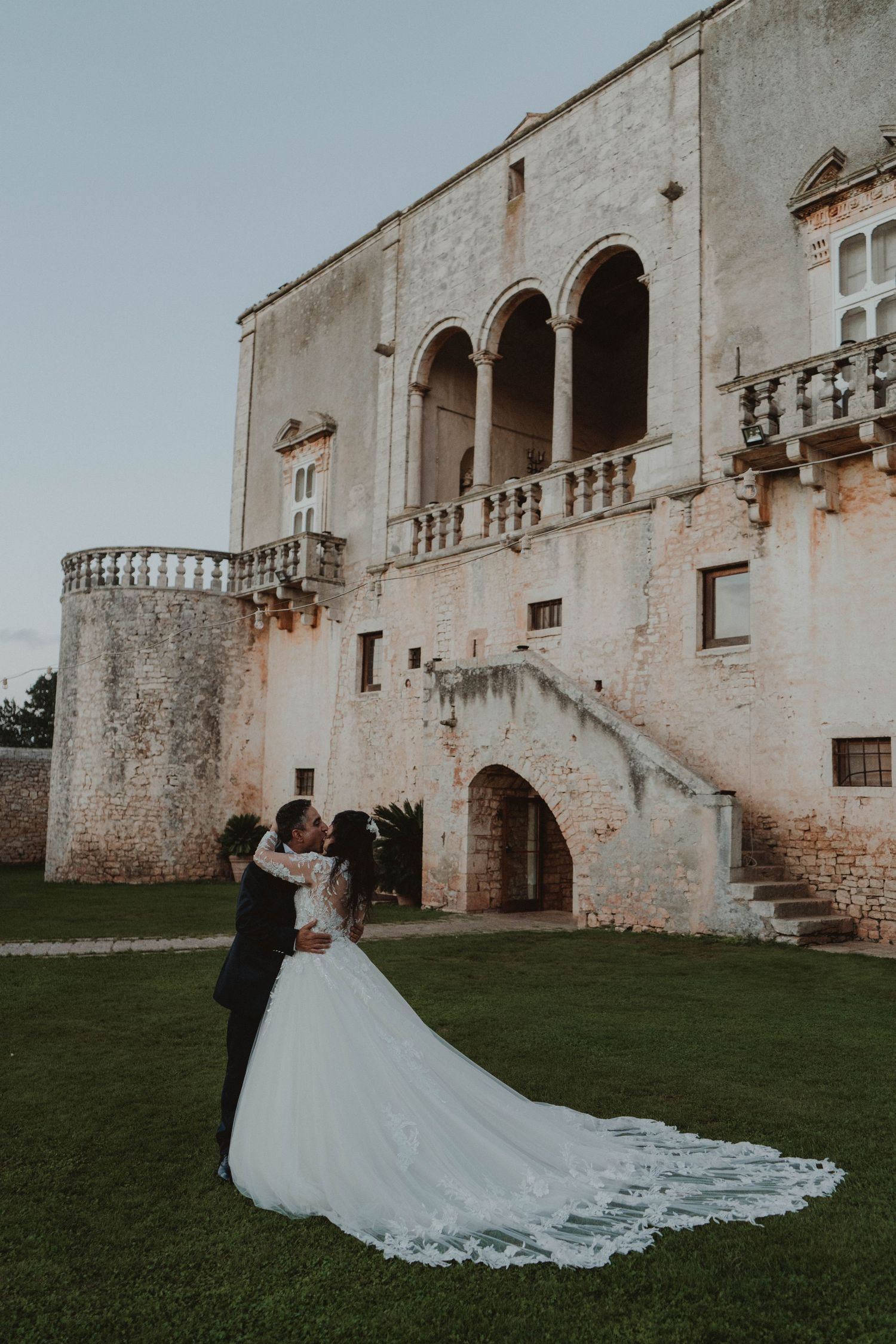 Couple standing in front of a historic castle in Puglia, Italy, at sunset on their wedding day.
