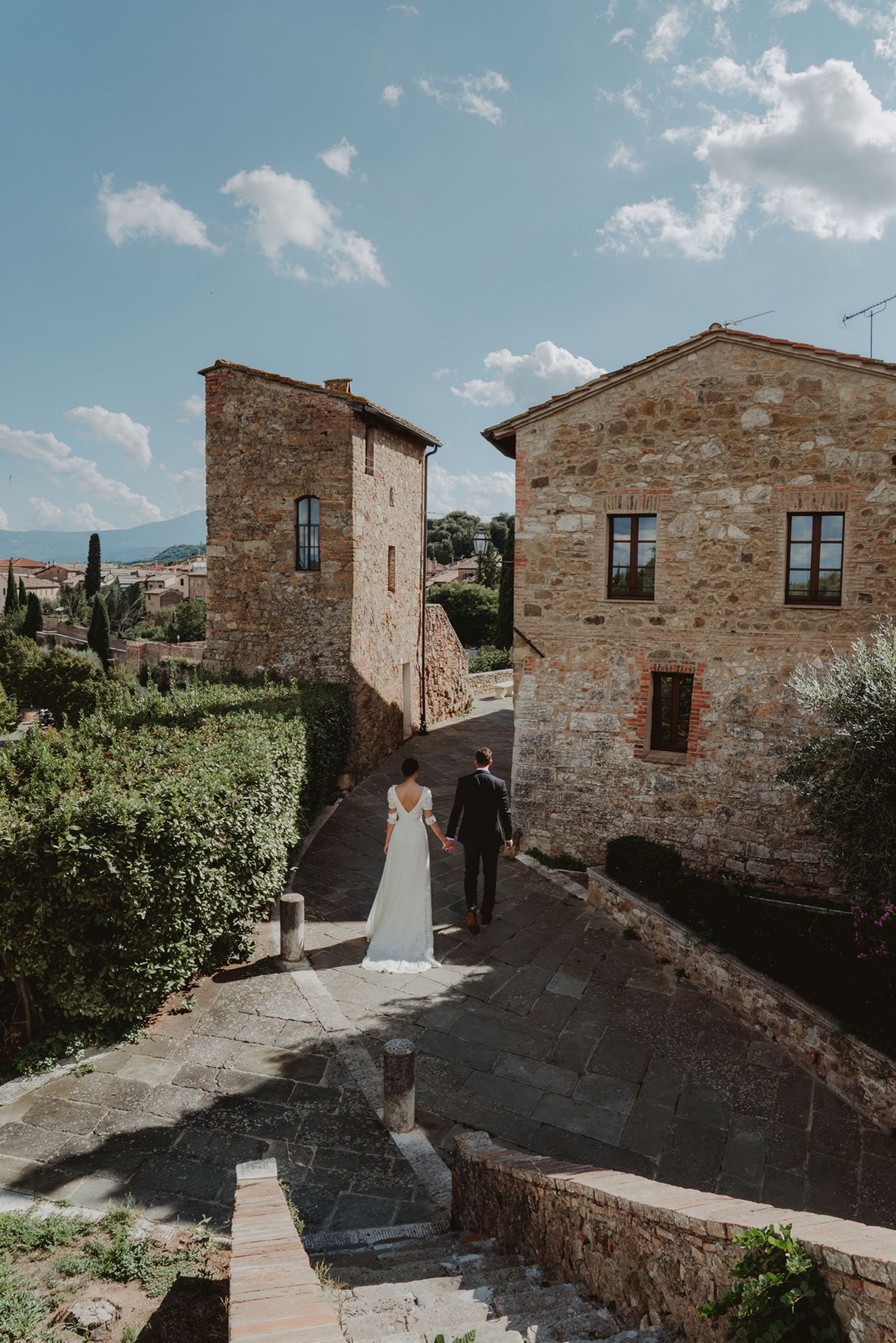 Newlywed couple walking away together as they enter a charming village in Tuscany, Italy, on their wedding day.