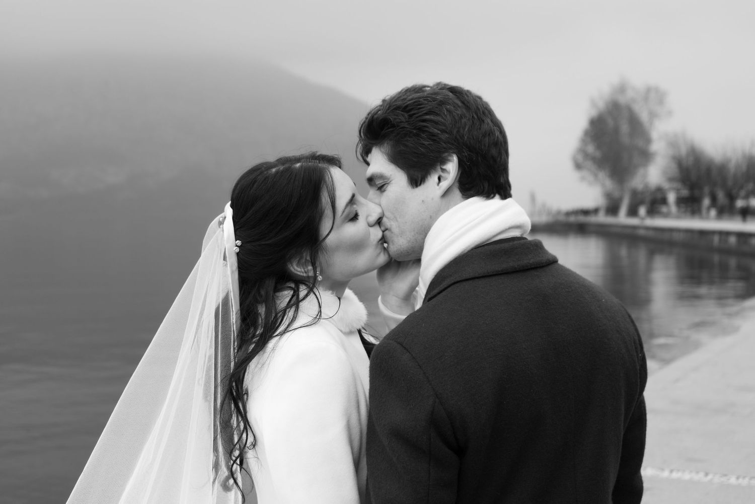 Newlywed couple kissing in front of a lake on their wedding day.
