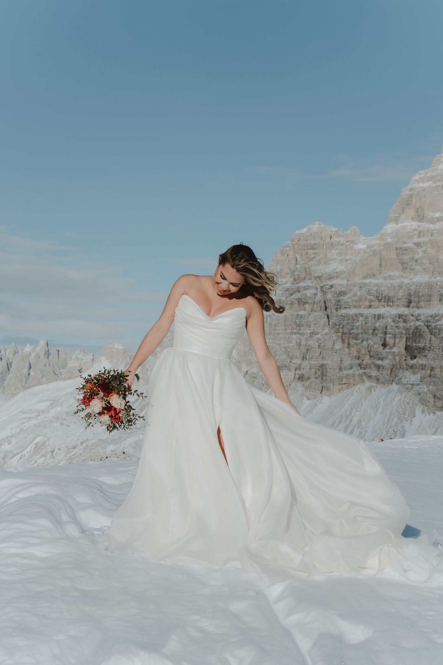 Bride standing on a mountaintop in winter, with her wedding dress flowing in the wind.