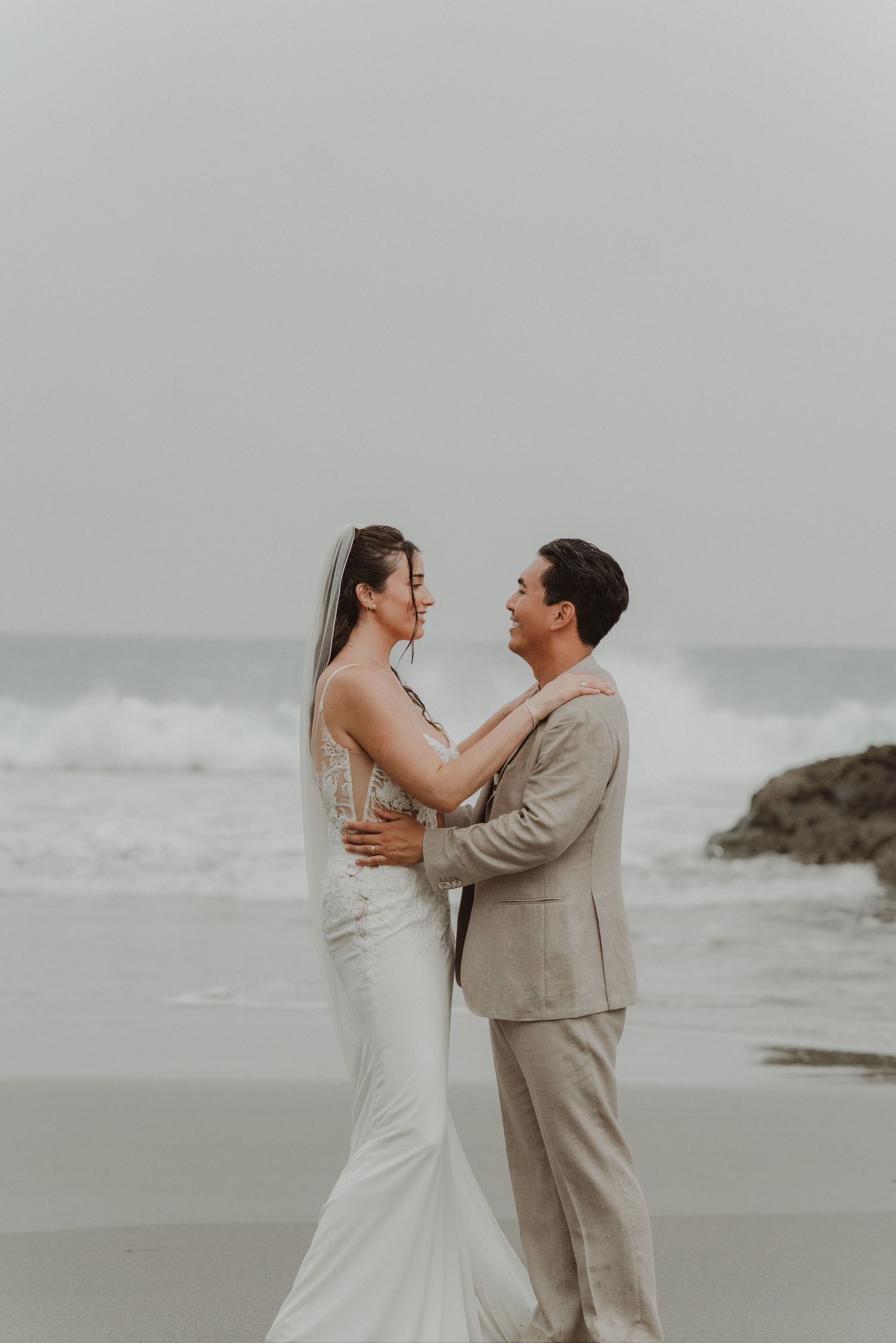 Newlywed couple looking at each other on a beach in Costa Rica, with waves breaking along the shore behind them.