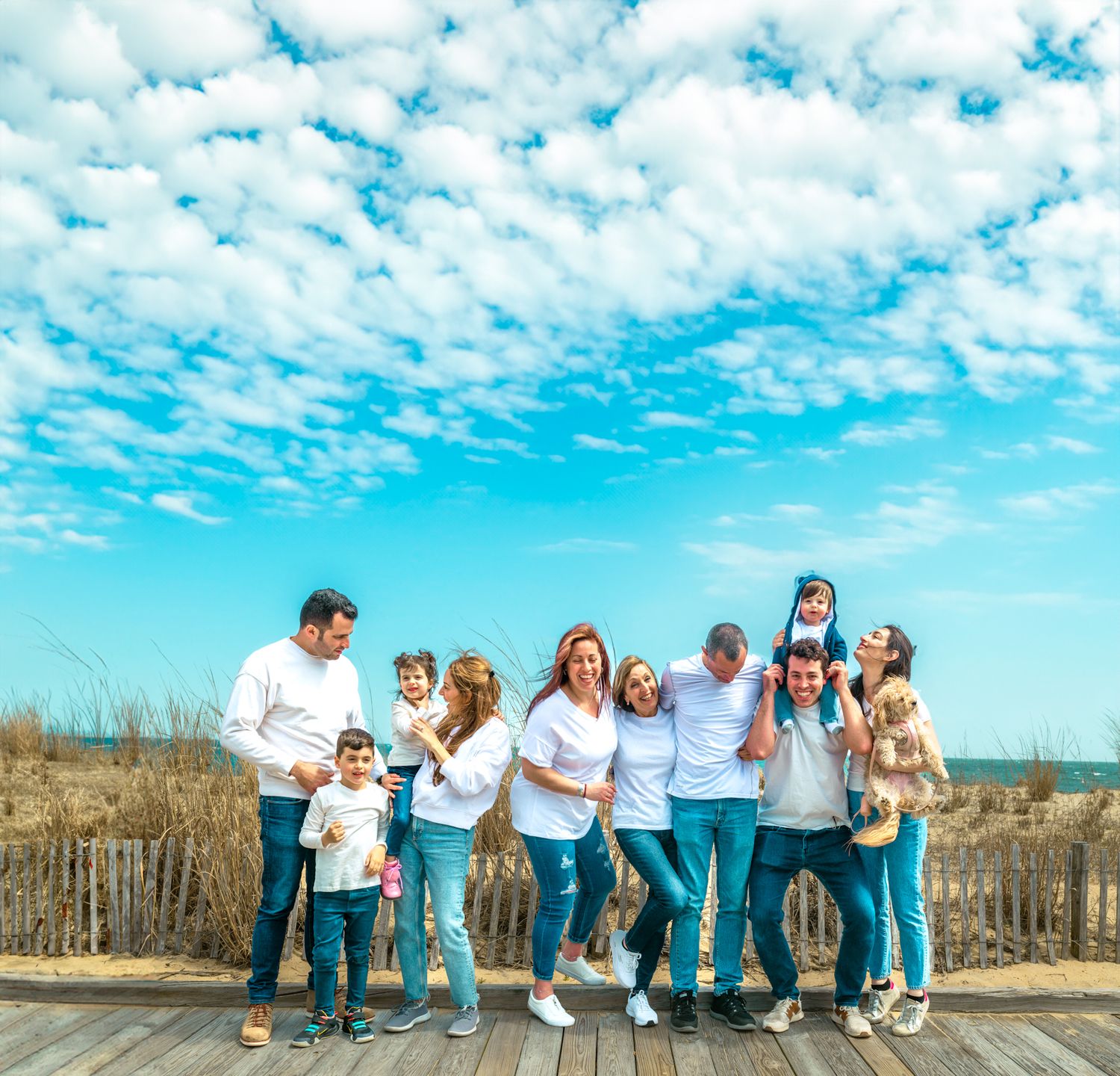 Large family group posing together on a beach boardwalk under a bright blue sky with fluffy white clouds.