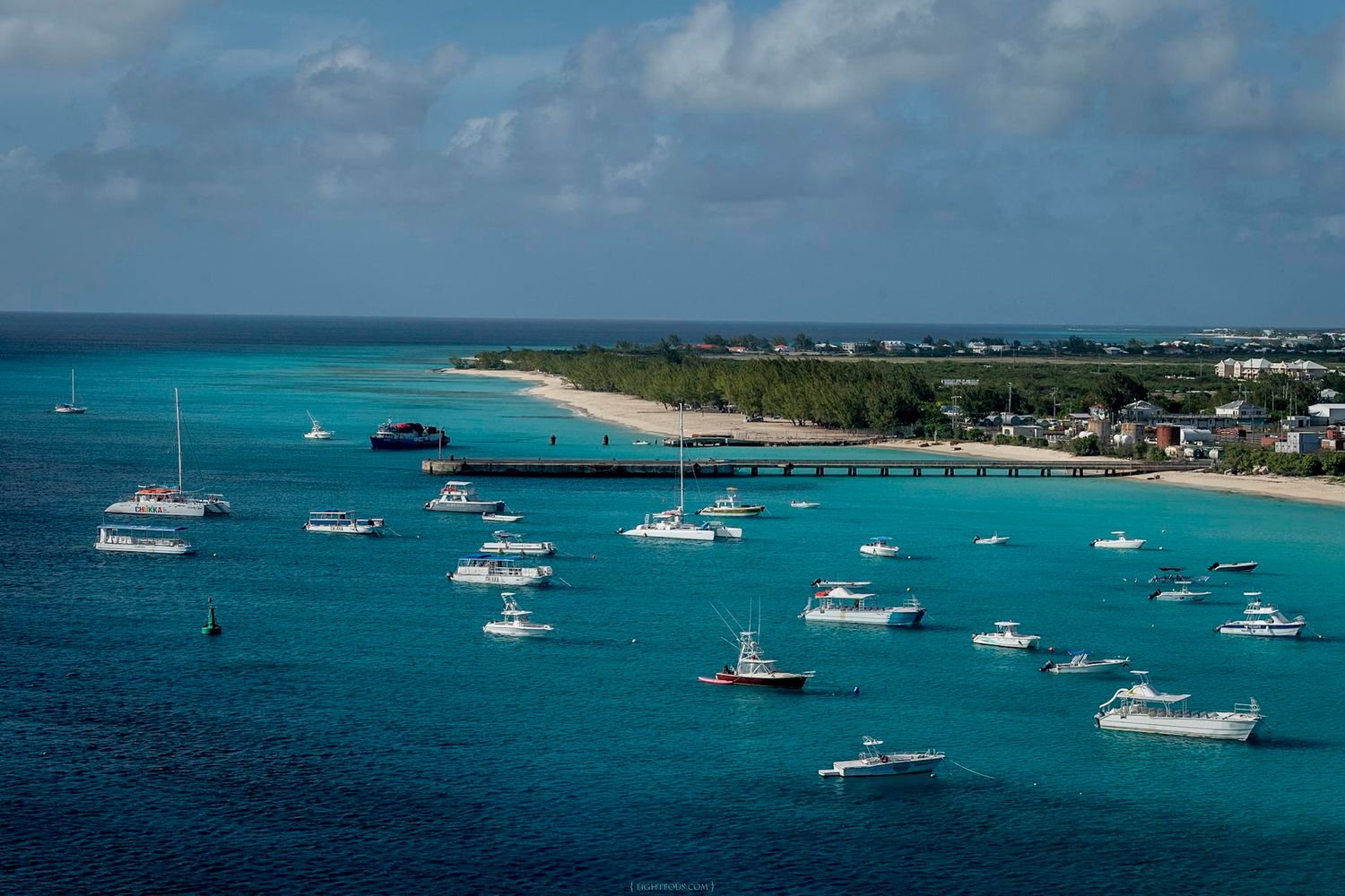 Aerial view of turquoise Caribbean waters with white boats anchored near a tropical island pier and sandy beach.
