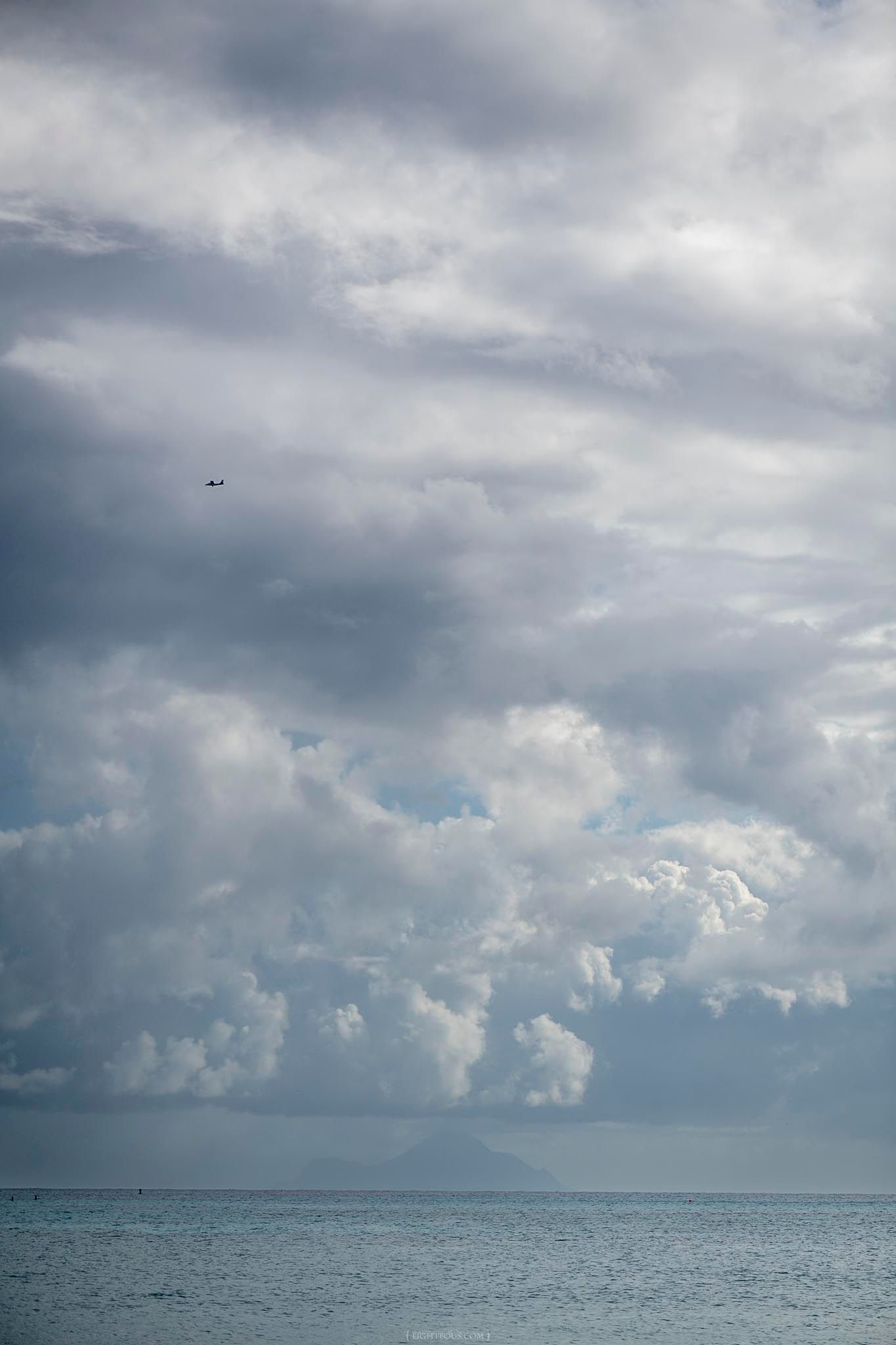 Dramatic stormy clouds over a calm ocean with a distant bird in flight.