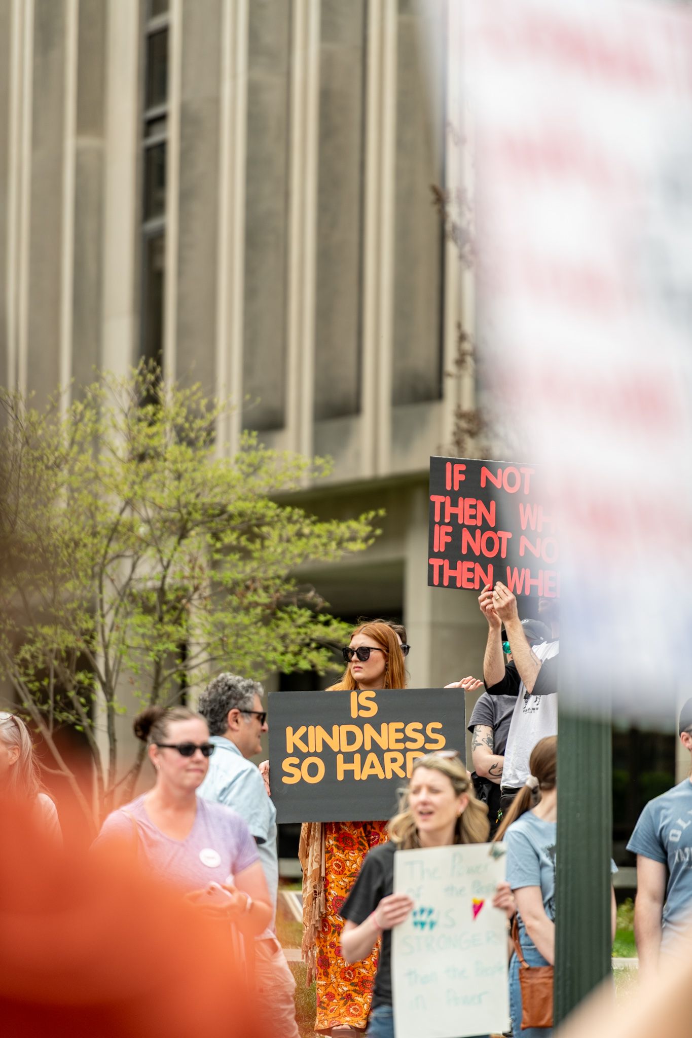Outdoor protest with signs about kindness visible among the crowd.