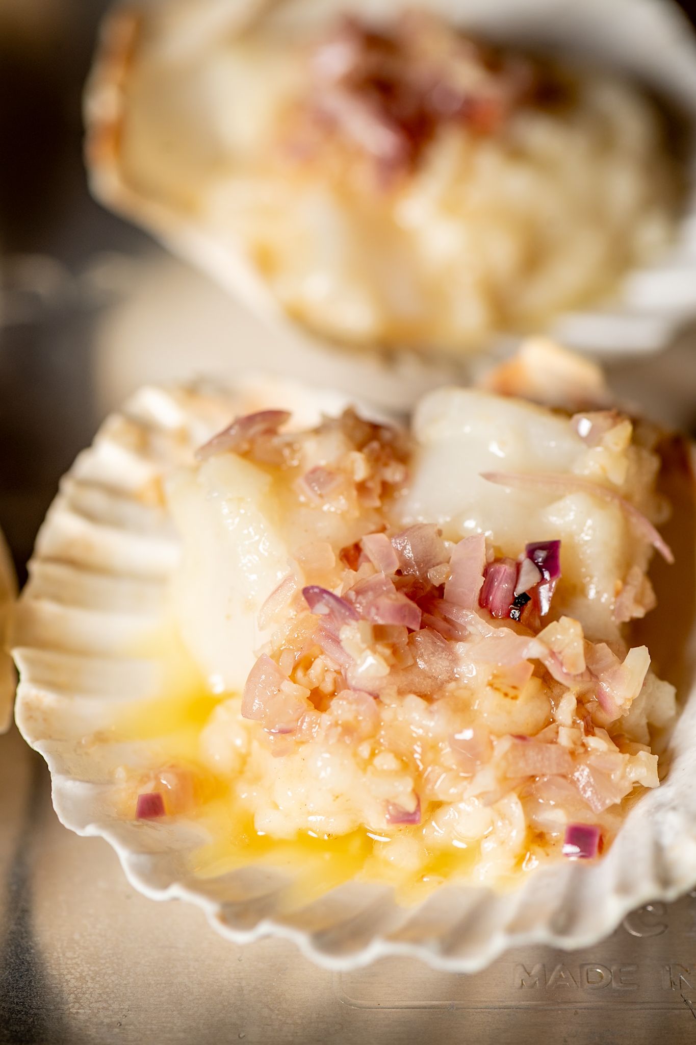 Fresh scallop in shell garnished with minced shallots and butter sauce.