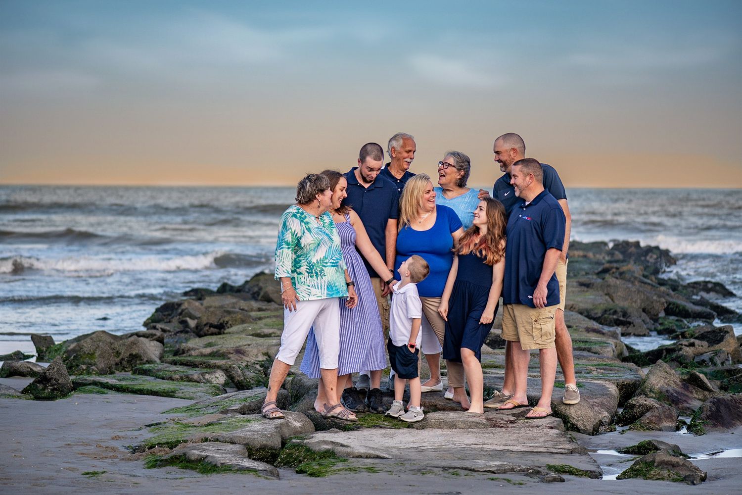 Family group portrait on rocky beach at sunset with ocean waves in background.