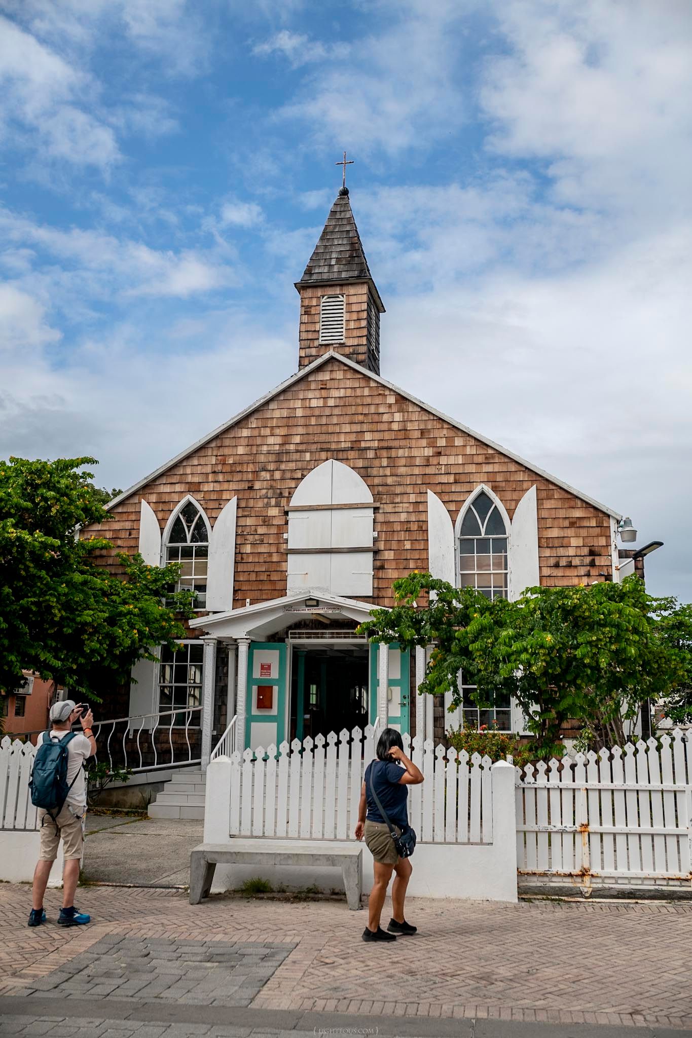 Historic wooden church with white picket fence and steeple in Key West, Florida, with tourists photographing outside.