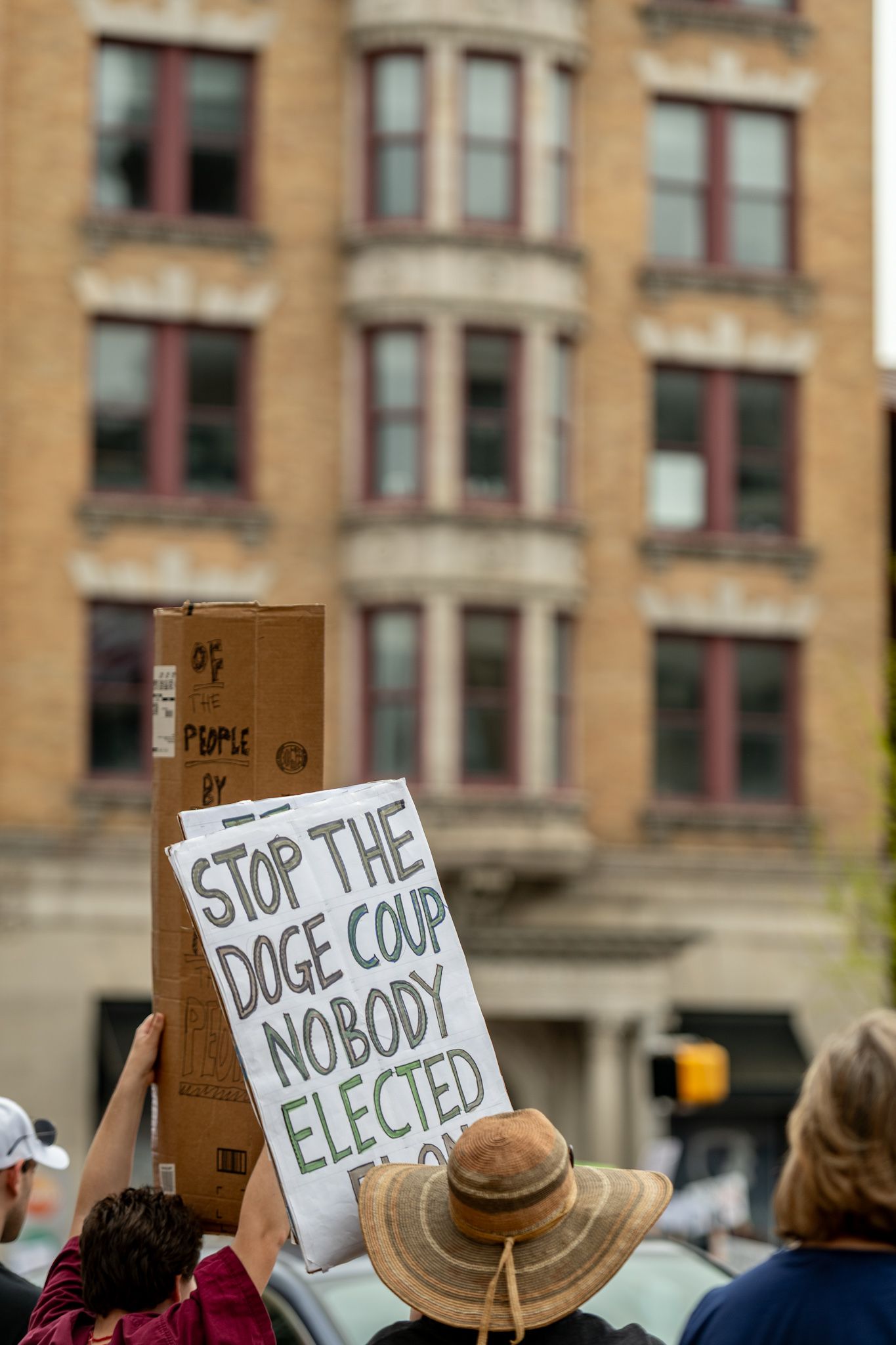 Protest signs held up against brick building backdrop during demonstration.