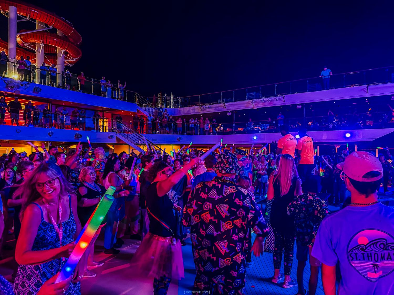 Colorful nighttime deck party on a cruise ship with glowing crowd, neon lights, and festive atmosphere.