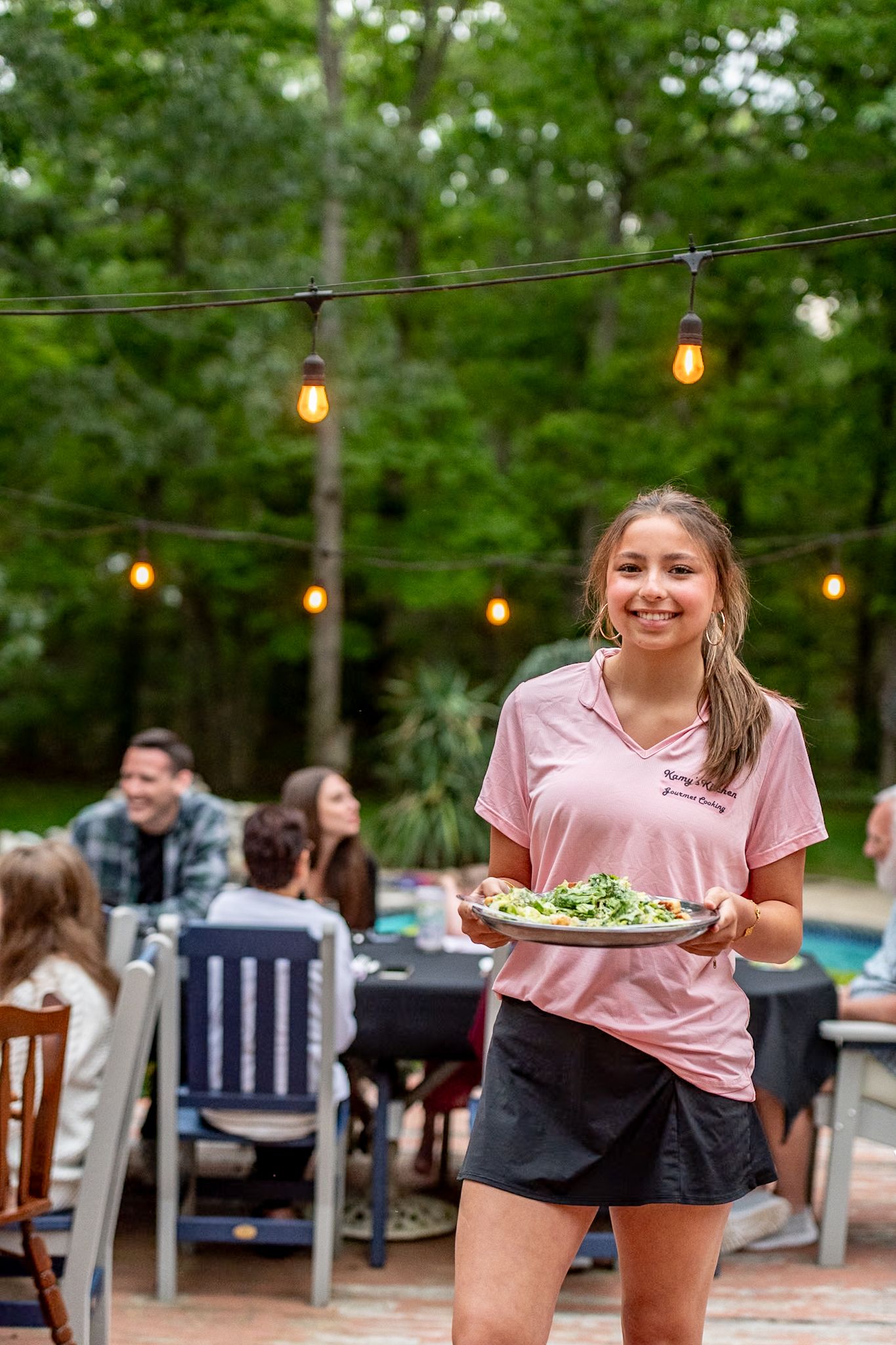 Outdoor dining scene with string lights and trees in background.