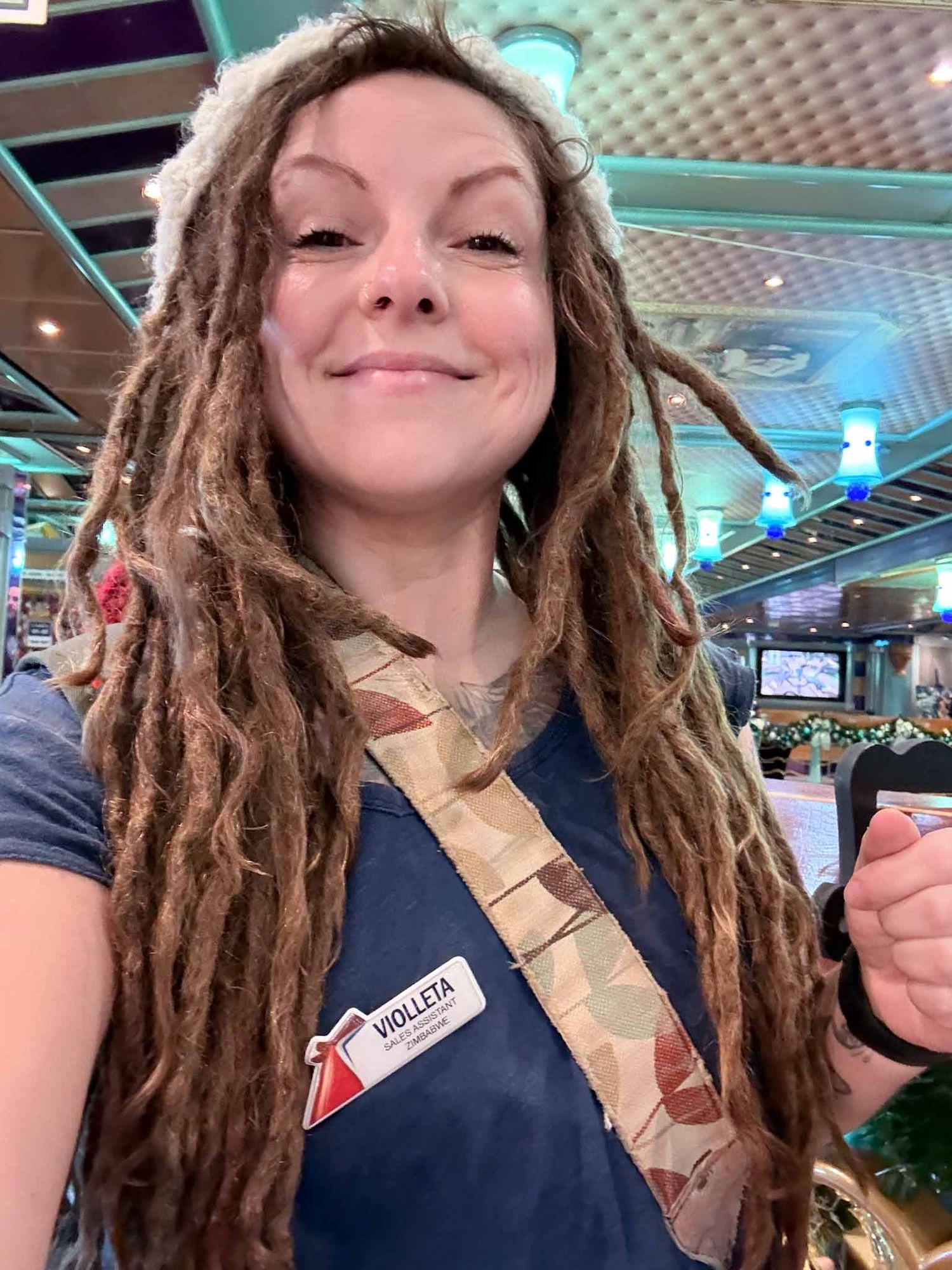 Person with dreadlocks wearing a dark shirt smiles and poses for a series of selfie photos in a restaurant setting.
