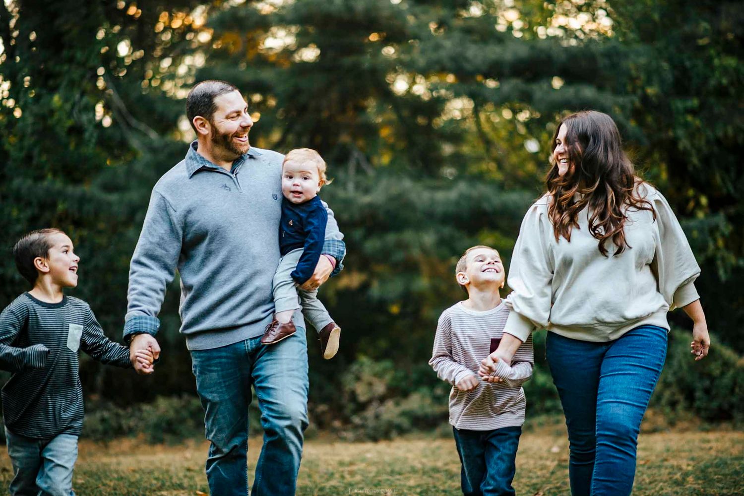 Happy family of five walking outdoors in autumn park, parents smiling with three young children among green trees.