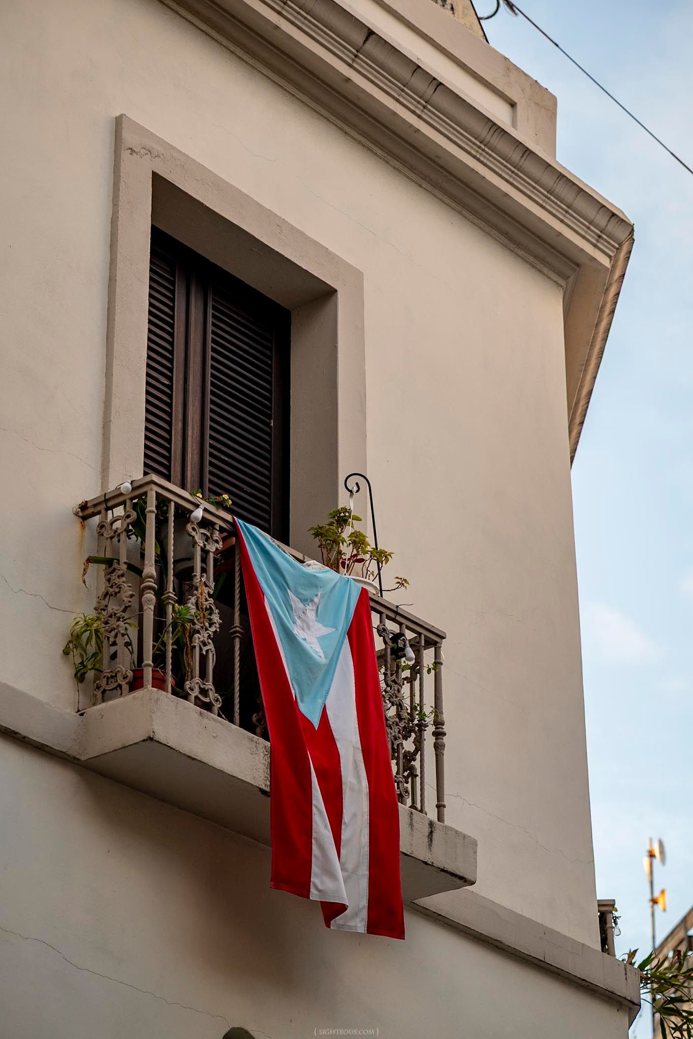 Puerto Rican flag hanging from a wrought iron balcony on a white colonial building in Old San Juan.