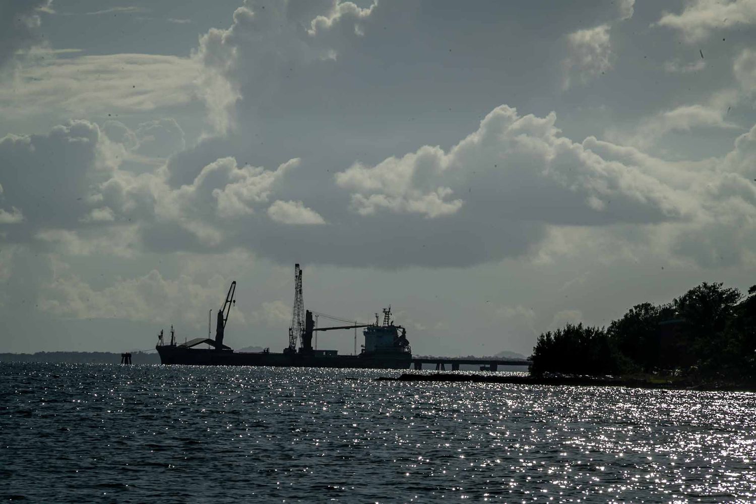Silhouette of boats on a glistening water surface against a dramatic cloudy sky.